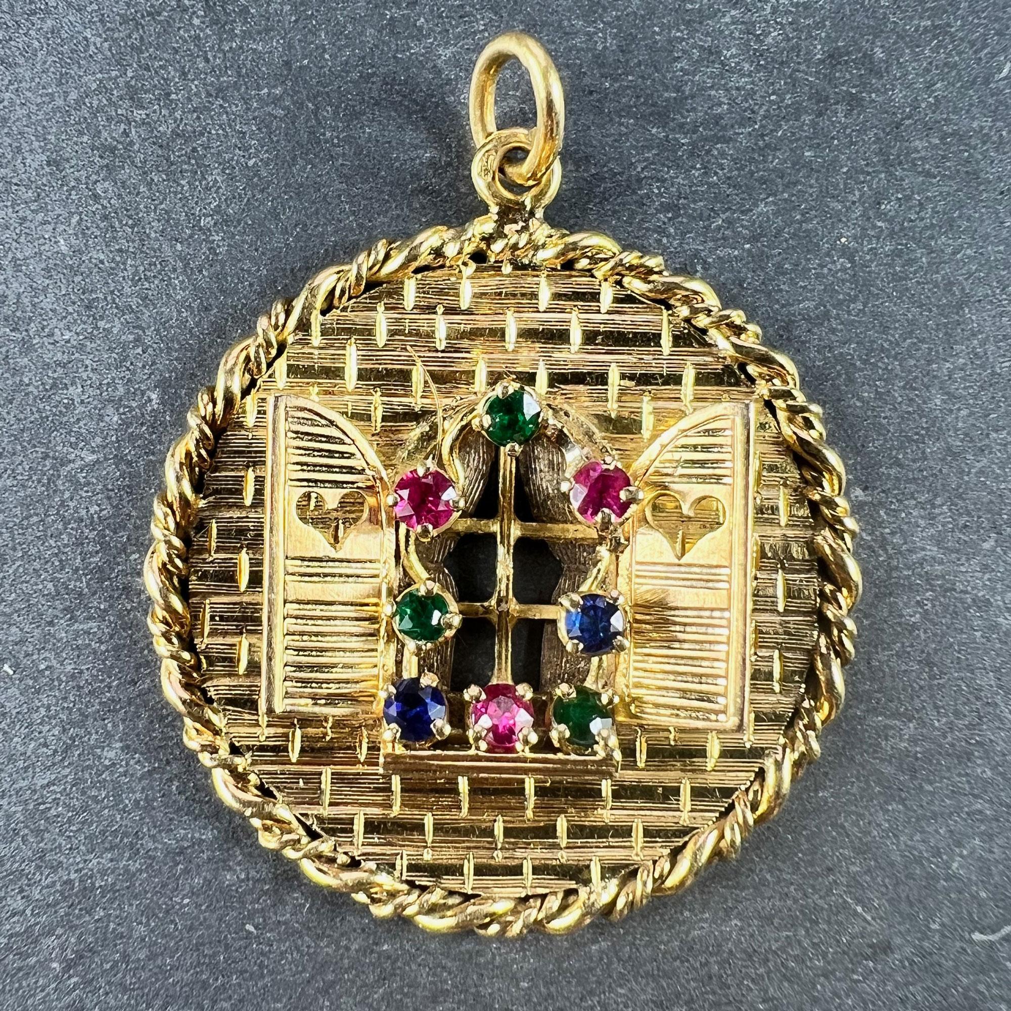 A French 18 karat (18K) yellow gold charm pendant depicting a window in a brick wall with open shutters with pierced love hearts. The windowbox and frame of the window are garlanded with flowers depicted by red, green and blue paste gems. Engraved