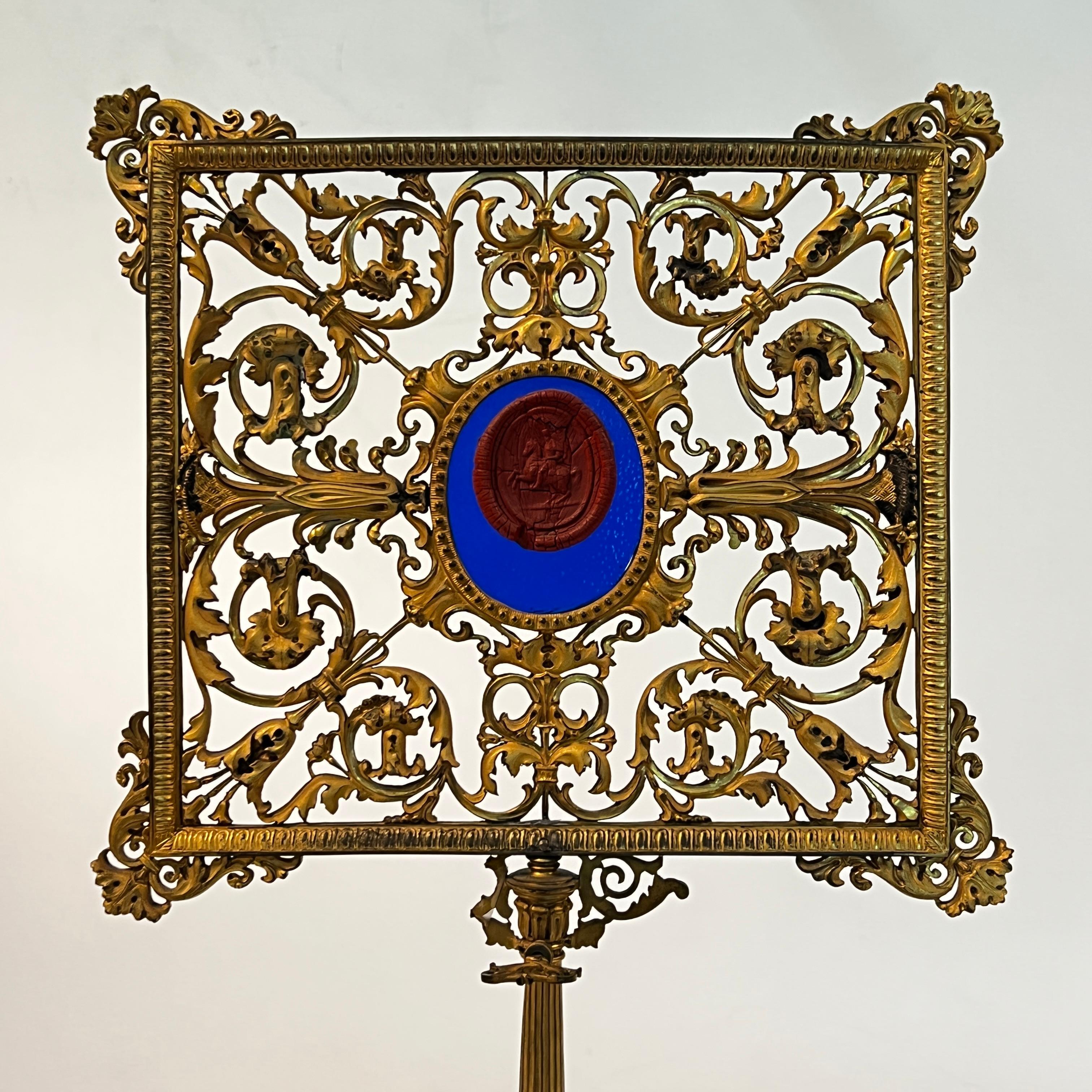 Our ormolu bronze table screen from the early 19th century is unique for its red wax seal depicting an officer on horseback, mounted to brilliant blue glass. Apparently unsigned and of French origin, based on the figure's tall cylindrical shako in