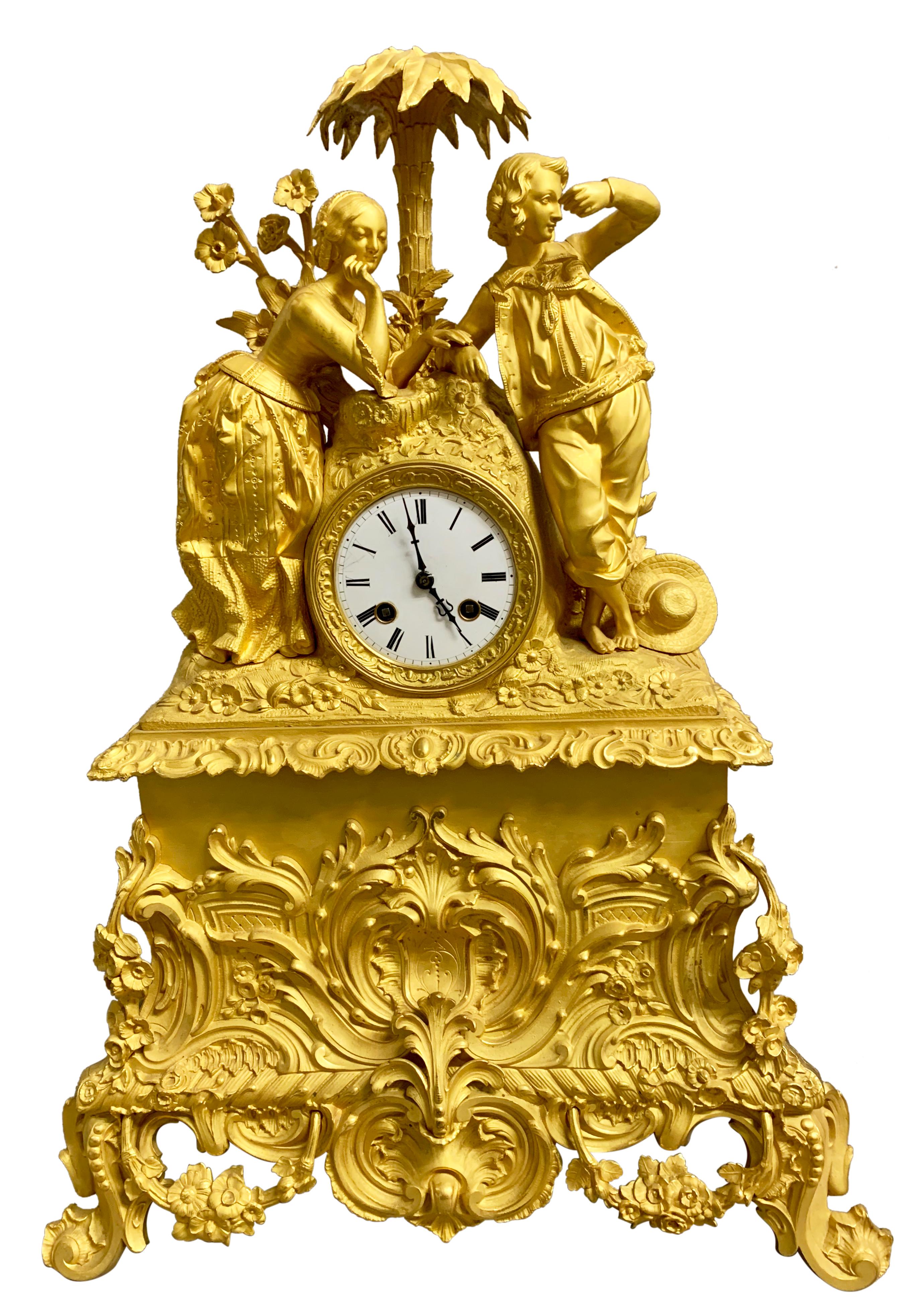 Pendule de cheminée en bronze doré d'époque Charles X. La caisse de tambour est flanquée d'un jeune couple debout sous un palmier avec des fleurs tout autour, tandis que la dame touche la main de l'homme.
La superbe et originale horloge en bronze