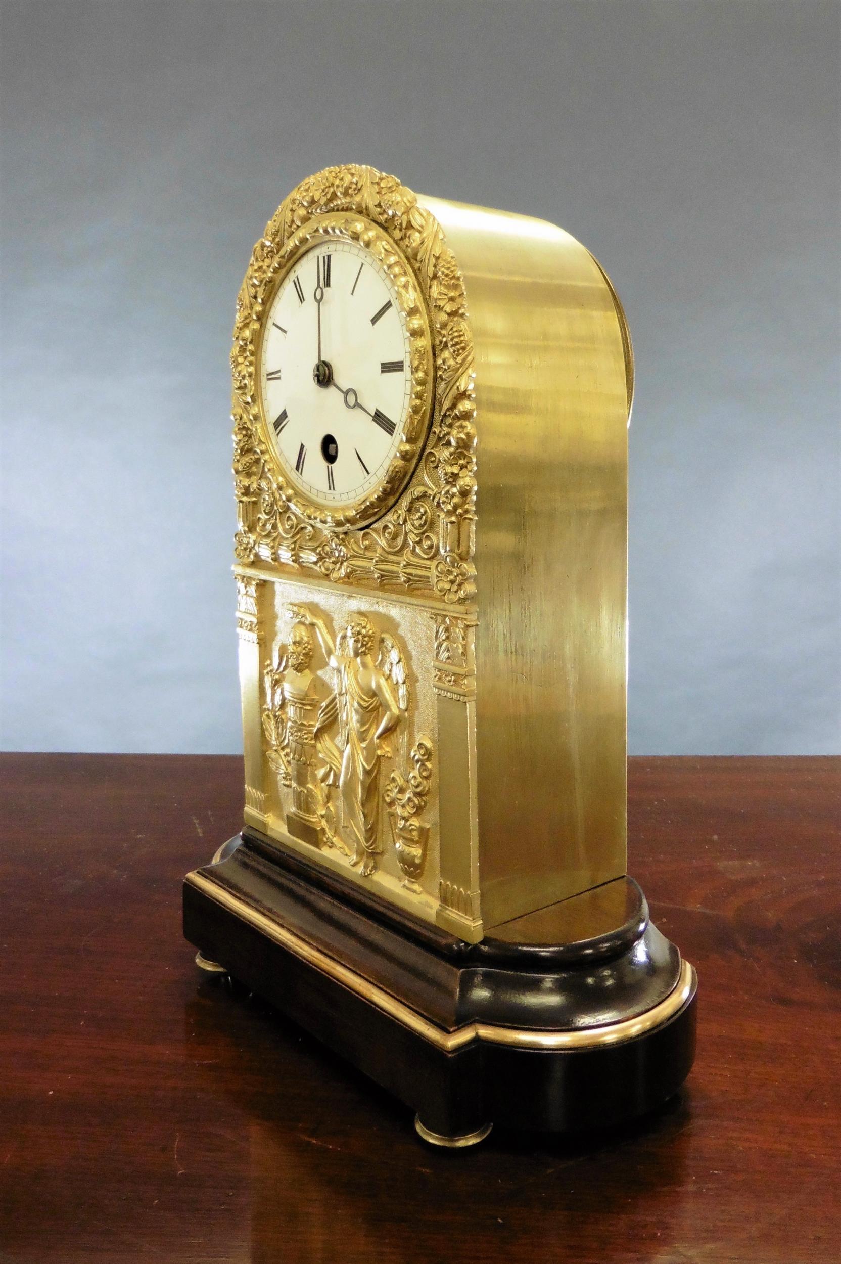 Arch top French mantel clock in a finely decorated Ormolu case with classical scene to the front, standing on a mahogany base with brass banding and resting on brass feet.

Enamel dial with Roman numerals and original ‘blued’ steel ‘Moonpoise’