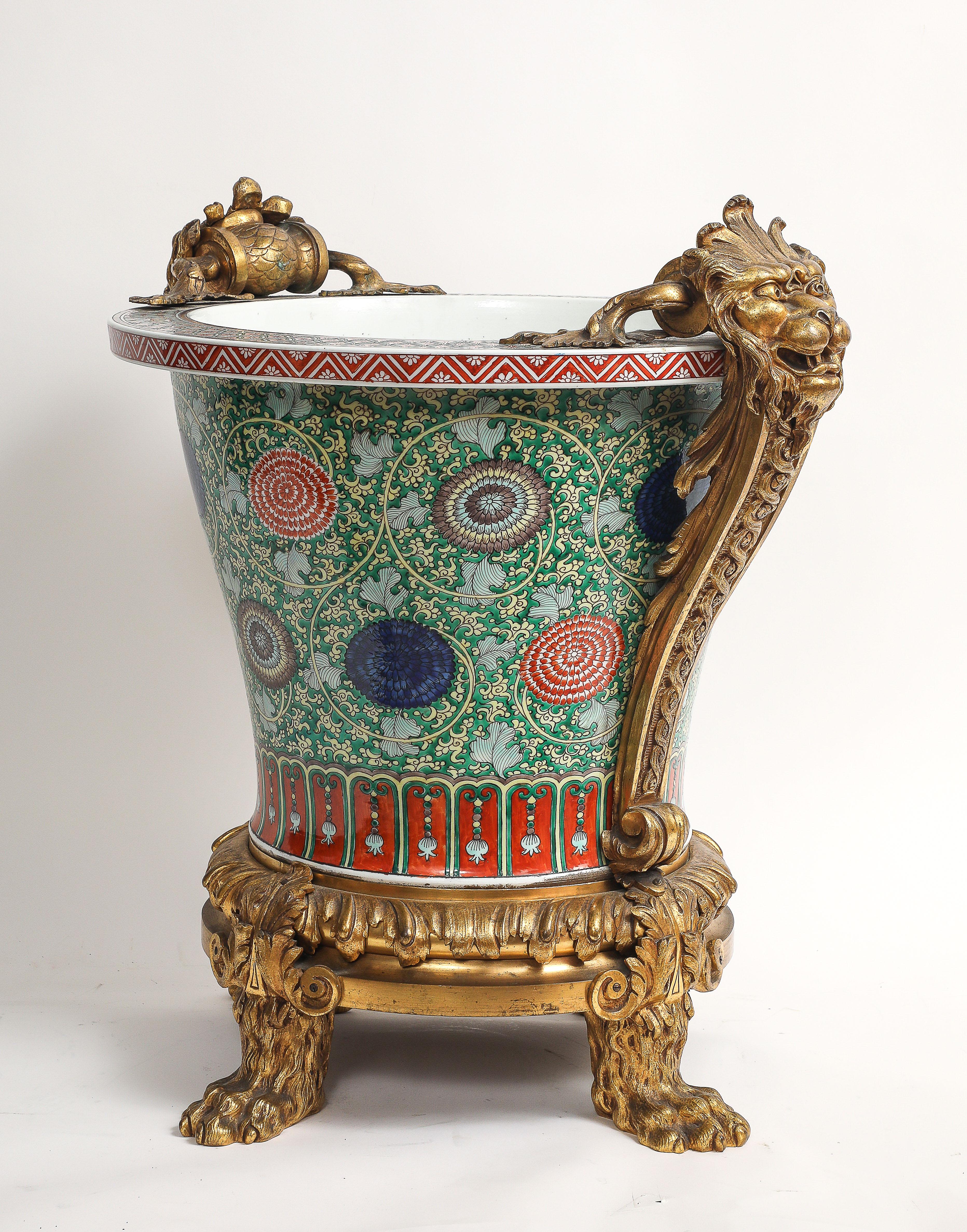 Un imponente Jardiniere/Planter/Centrotavola/Secchiello da champagne in porcellana cinese Famille Verte con manici a forma di maschera di testa di leone in Ormolu. La jardiniere è di grandi dimensioni, con un corpo ampio e svasato e un bordo largo,