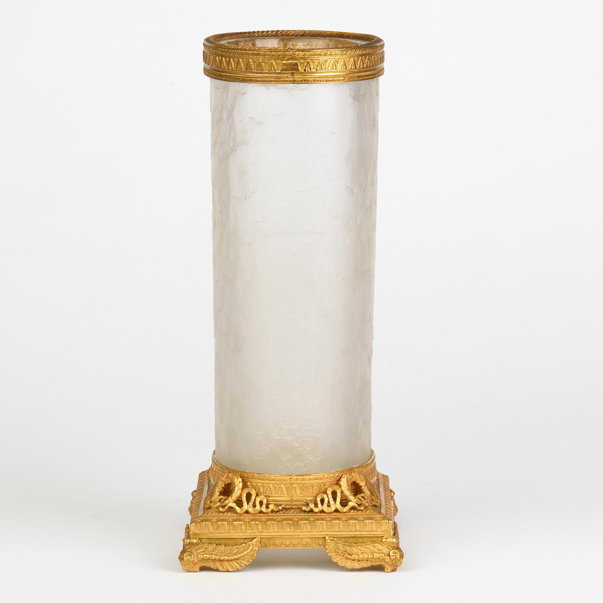 A fine antique French ormolu-mounted sleeve shaped glass vase of cylindrical form with a finely frosted and textured finish with raised gilded mount finely detailed with open work ribbon and winged ram head feet with a gilded and patterned metal rim