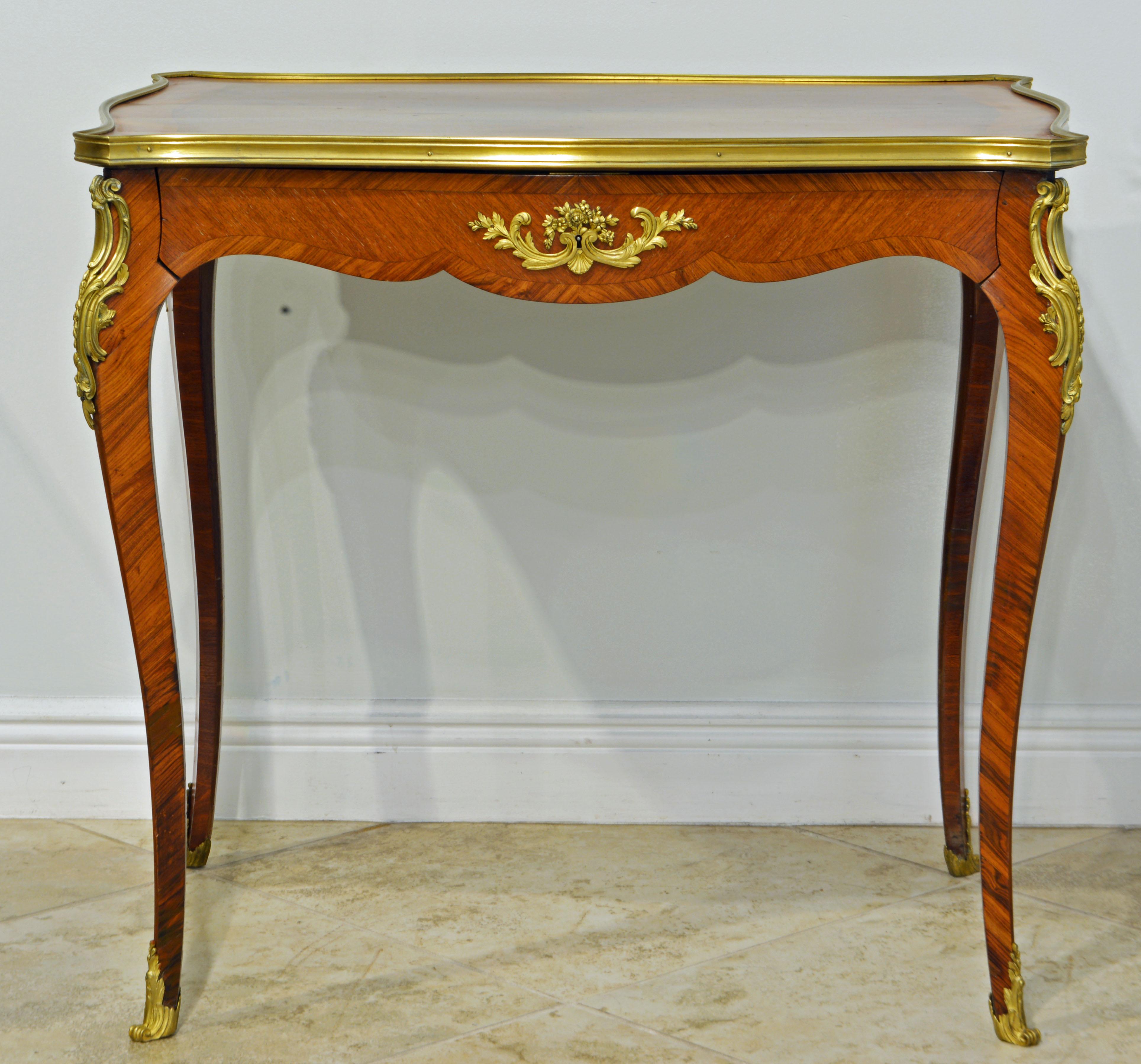 This elegant side table features a parquetry shaped top surrounded by a gilt bronze edge above shaped aprons accented by elaborate gilt bronze mounts on the corners and centered bronze mounts on all for sides. The apron offers a concealed long