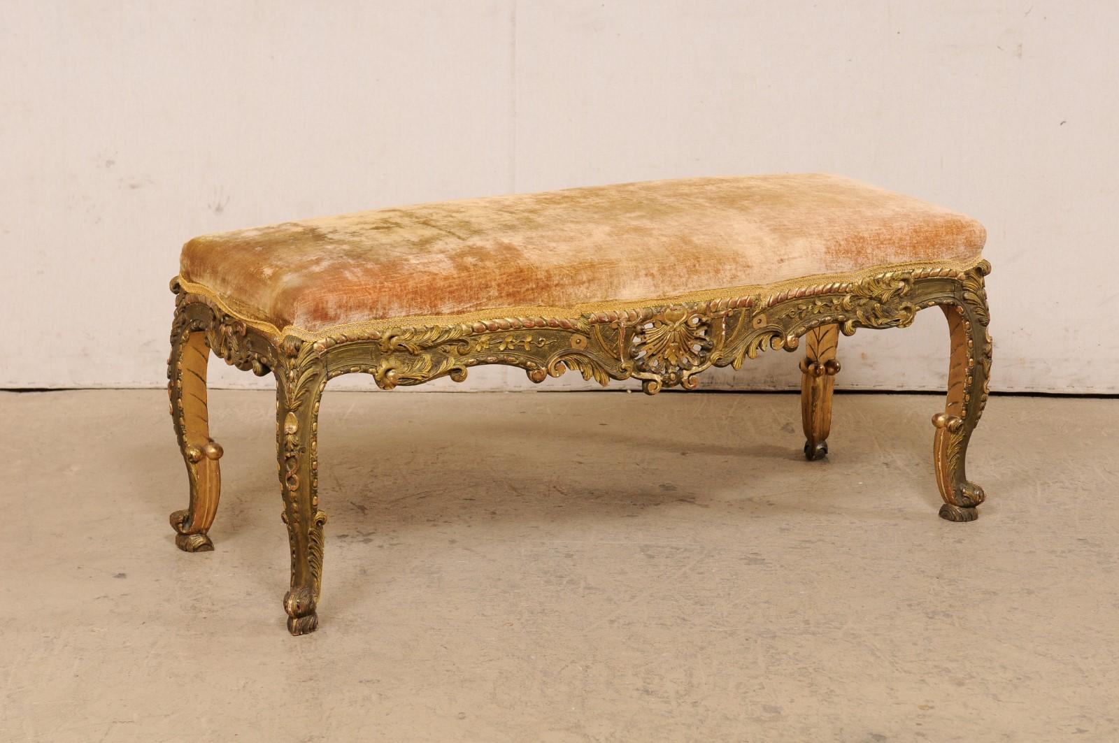 A French carved and gilt wood bench with upholstered seat from the late 19th century. This antique bench from France has a mostly rectangular-shape with curvy serpentine profiled sides. The upholstered seat is framed within an elaborately carved