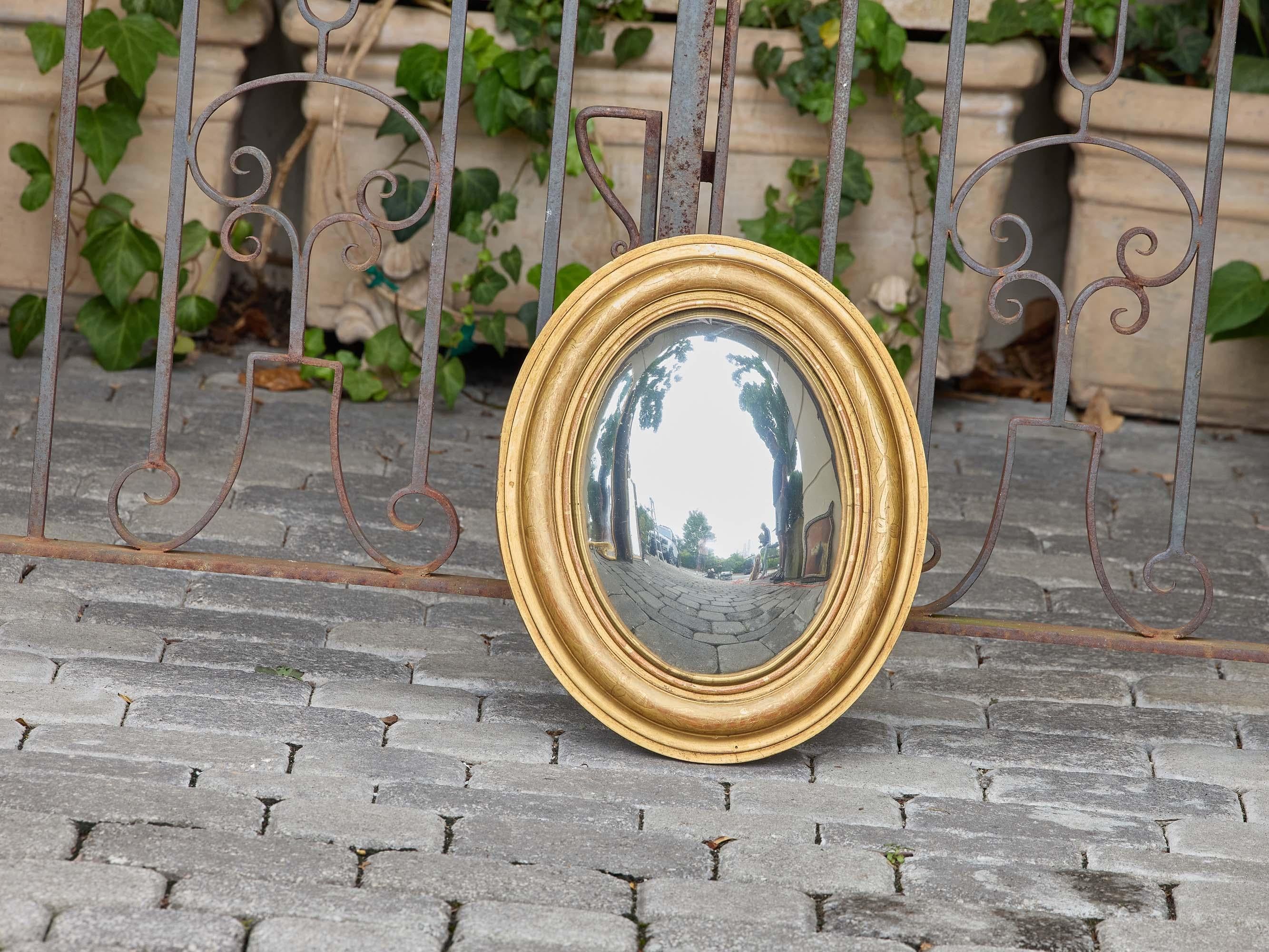 Miroir convexe ovale français datant de 1920 environ, situé dans un cadre en bois richement doré. Le cadre est moulé dans une forme ovale douce avec une sculpture en couches, sa surface dorée offre une patine chaude et usée par le temps qui rehausse