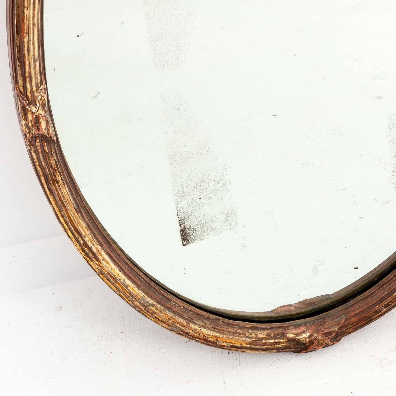 This exquisite French giltwood oval mirror from the early 20th century epitomizes timeless elegance and craftsmanship. Adorned with gilded details, the frame exudes opulence and sophistication. Its crowning glory is a gracefully sculpted bow, adding
