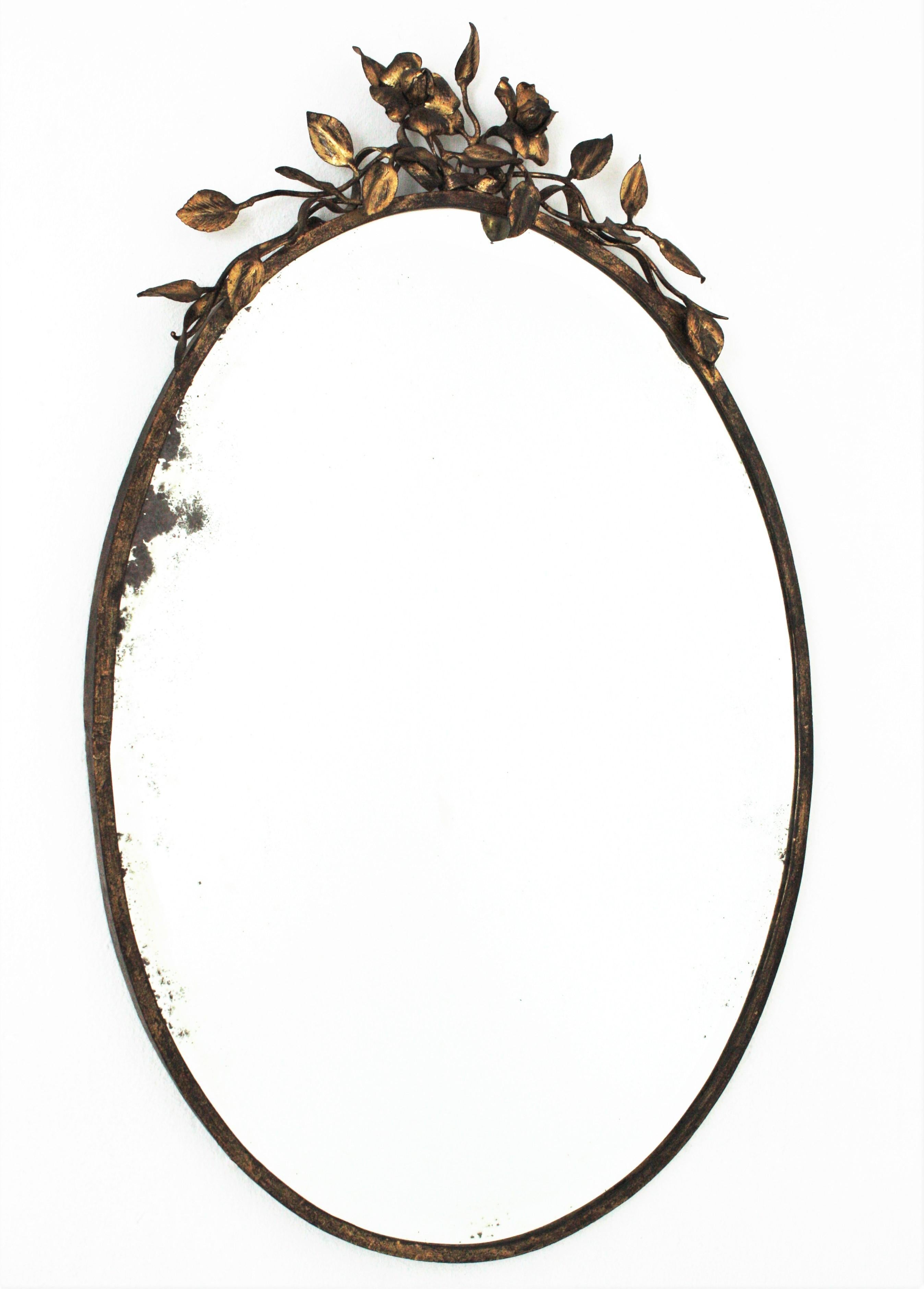 Oval mirror with foliage floral crest, gilt iron, gold leaf, beveled glass. France, 1940s
Elegant oval mirror with floral details on the top. 
Terrific aged patina and original beveled glass mirror.
It will be a nice addition to a powder room,