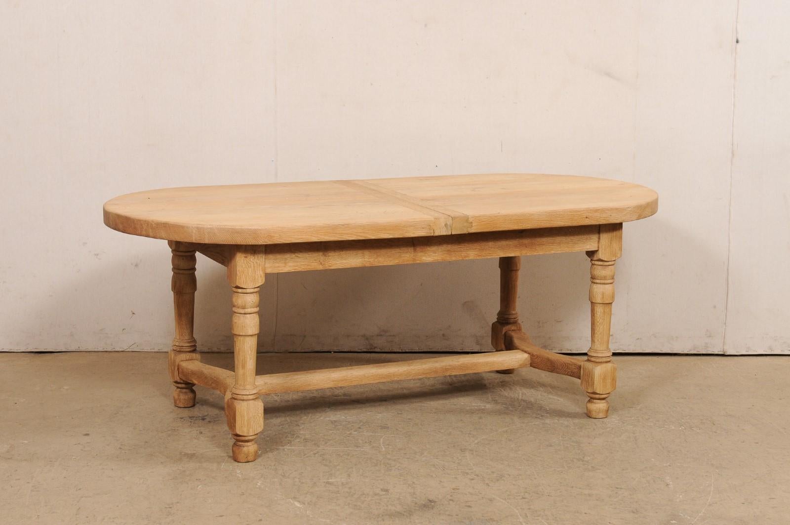 A French oval-shaped wooden table from the mid 20th century. This mid-century table from France has an oval-shaped top, which rests atop a plain apron, and raised upon four baluster-style carved legs. The legs are braced within a wood beam