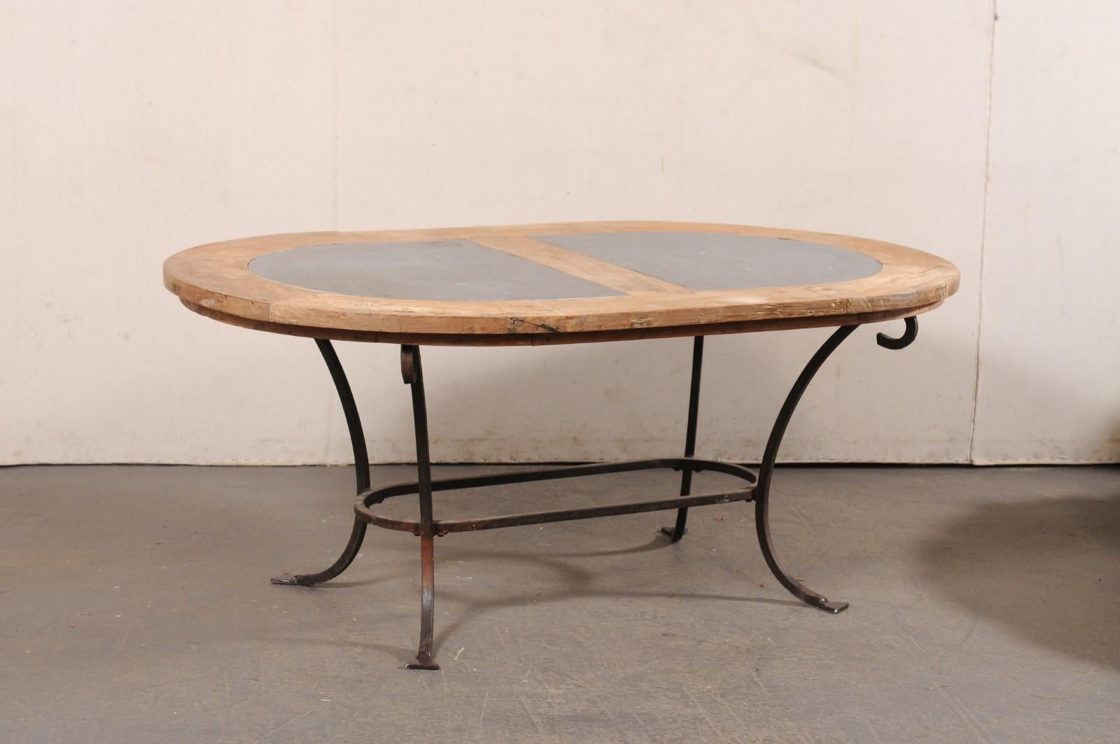 A French wood and stone table with iron base from the mid 20th century. This mid-century table from France has an oval-shaped top wooden top with two sections of stone inlay, which is raised upon a forged-iron base with four c-scroll shaped legs