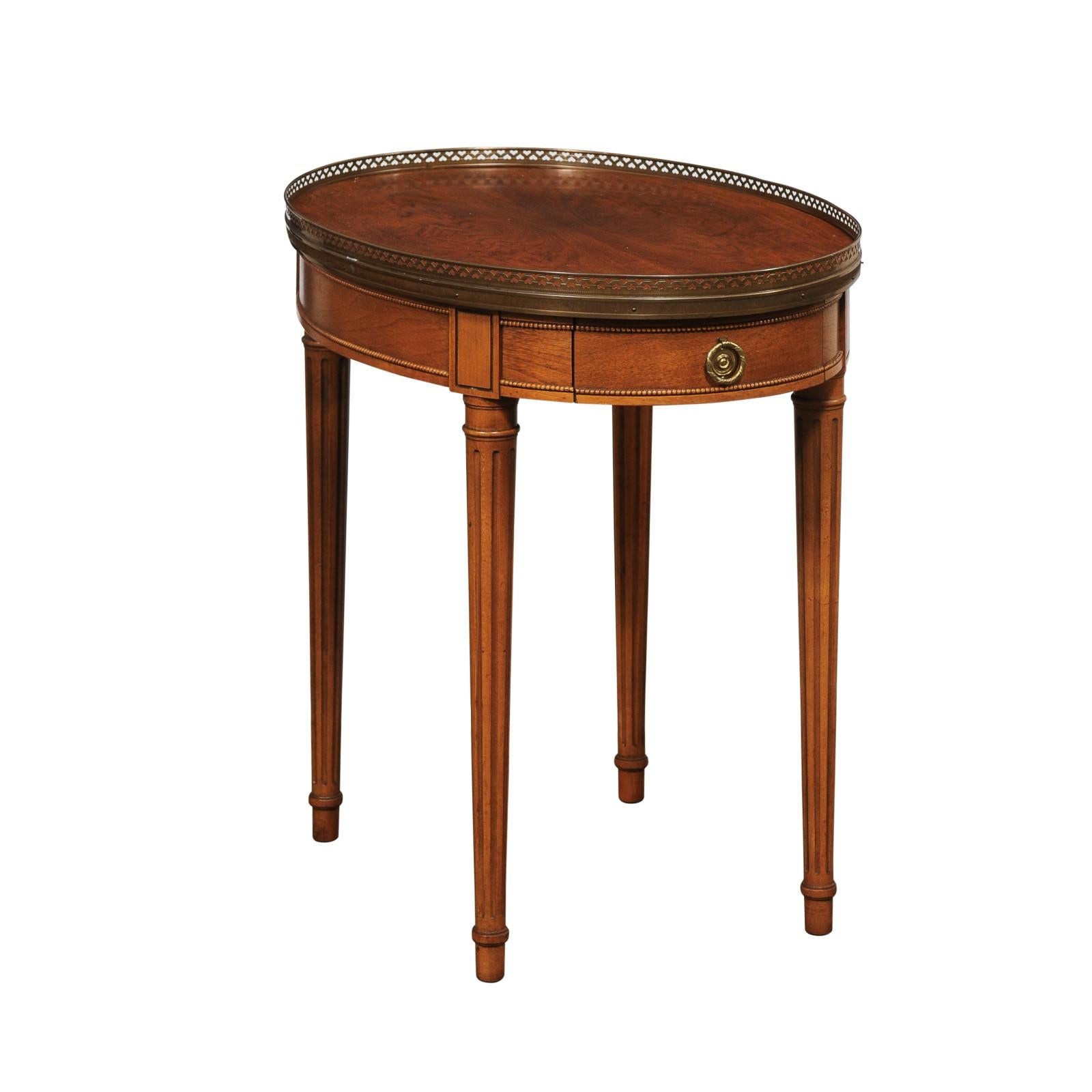 A French accent or side table with brass gallery edge top, from the mid 20th century. This vintage smaller-sized table from France is oval in shape, with top outlined in a raised gallery style brass lip. The apron houses a small drawer and the front