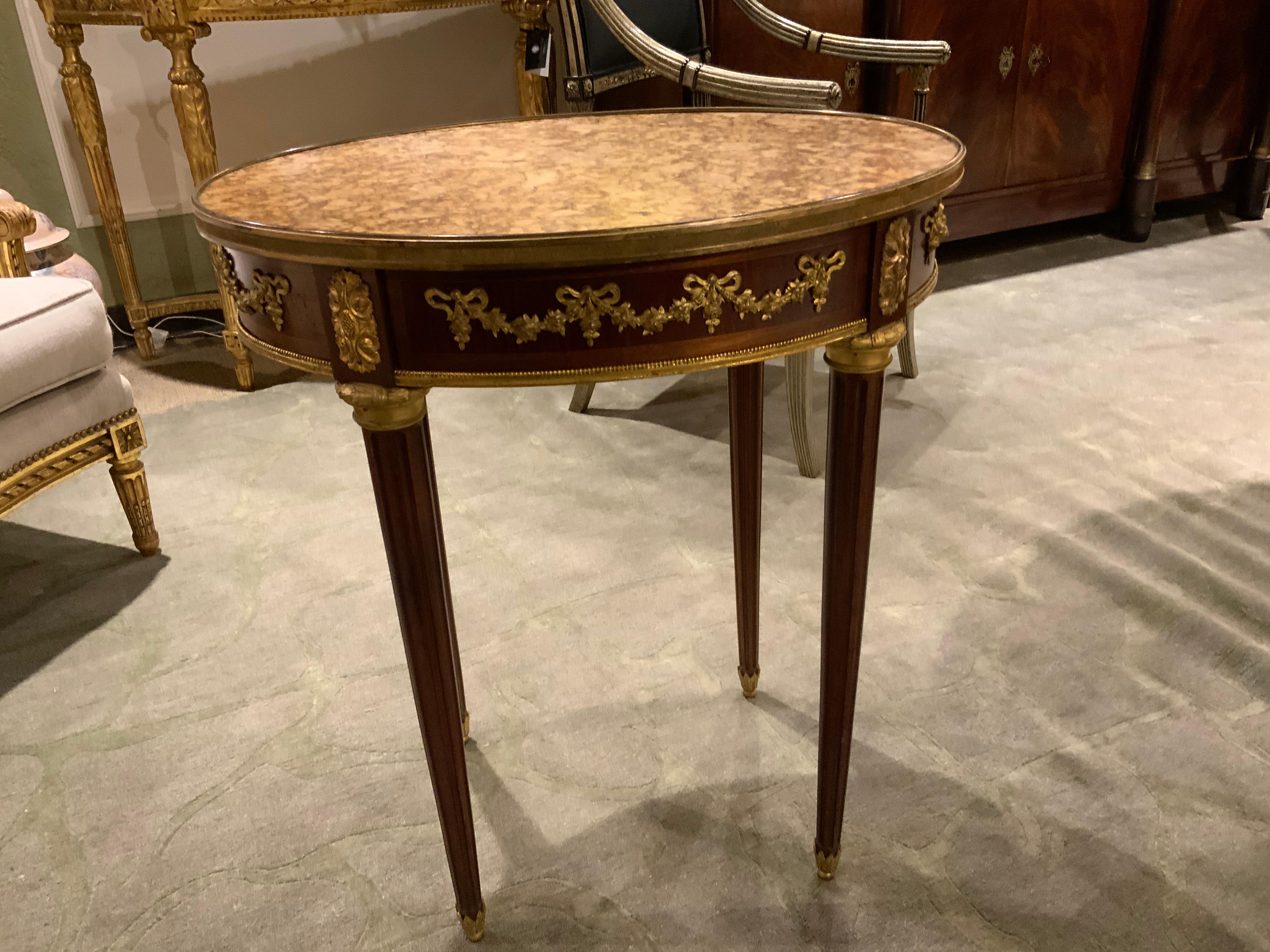 Exquisite oval table with gilt bronze swags depicting bows and floral swags. Having a gold mingled
Marble inset at the top, rimmed in gilt bronze. Reeded legs ending in sabots.