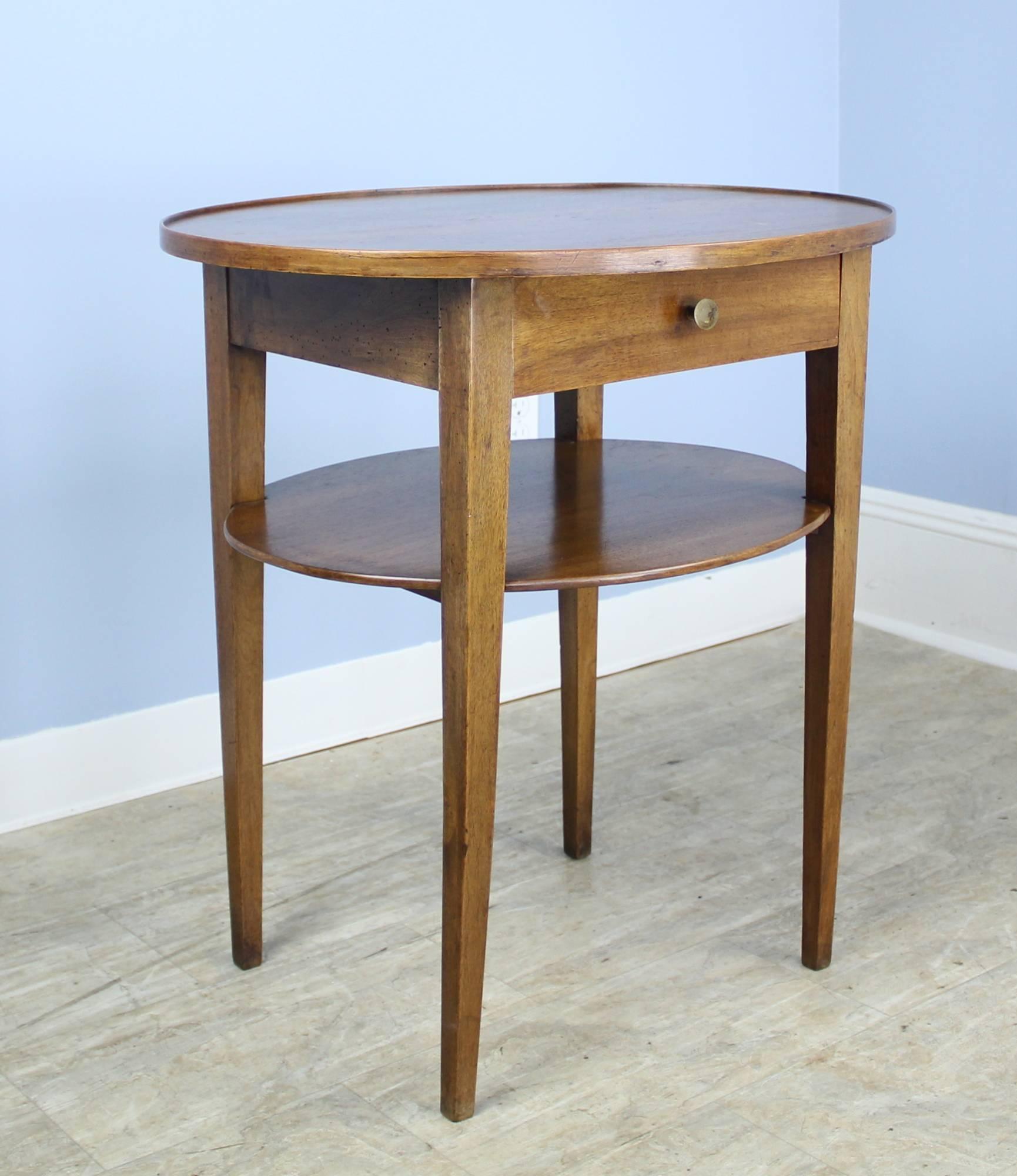 An elegant oval walnut side table with an unusual lower shelf. Single drawer, tapered legs, and a small galleried edge complete the look.