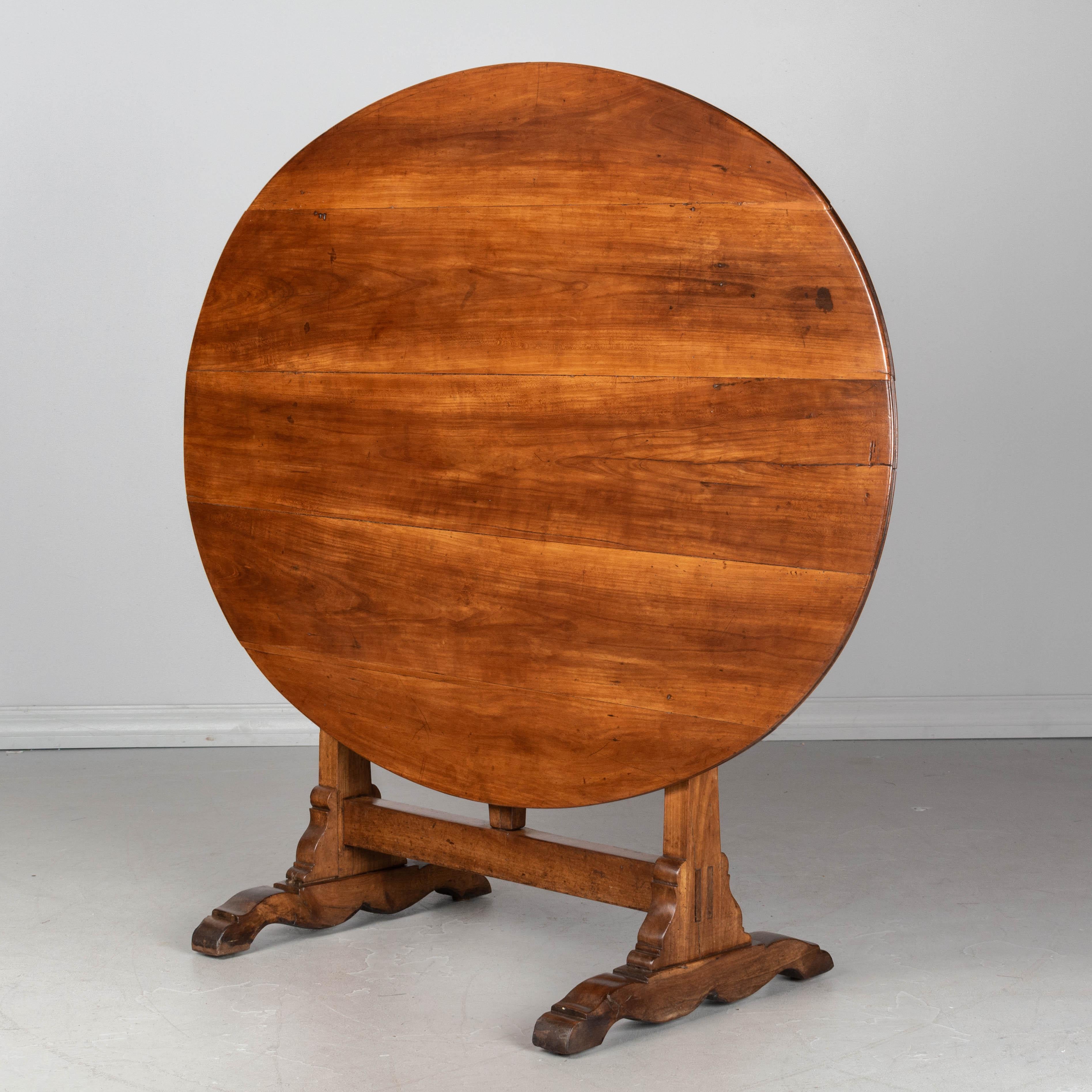 A French wine tasting, or tilt-top table, made of solid cherrywood. Oval top with sturdy trestle base. Legs have nice decorative form. Well-crafted with mortise and tenon joints and pegged construction. Good restored condition. Waxed
