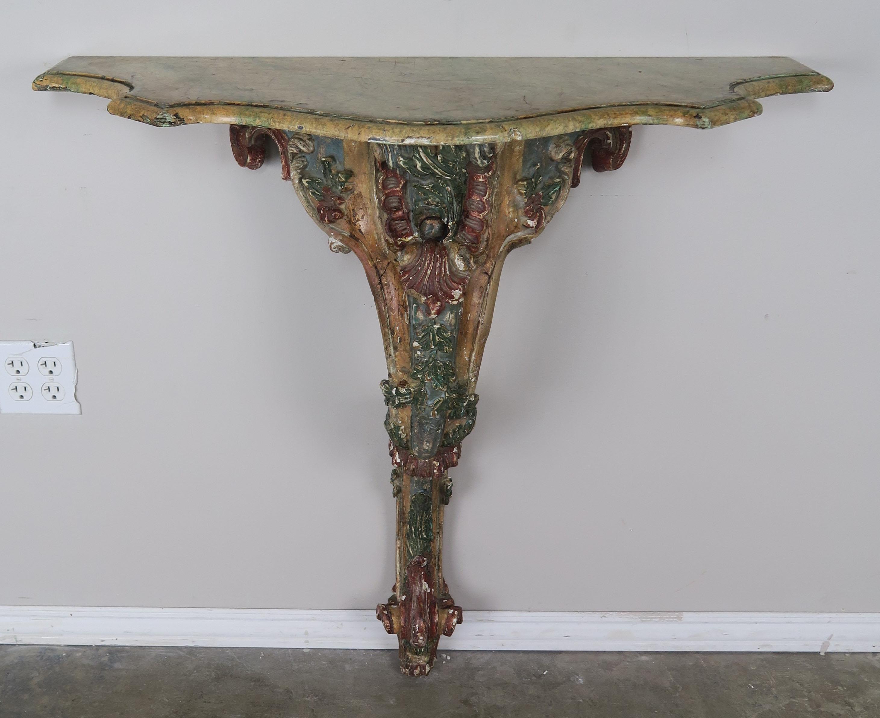French painted carved console with serpentine shaped top. The console stands on a single cabriole leg that ends in a ram's head foot. The console is painted in distressed shades of green, gold and rust. A serpentine shaped top with a nice edge