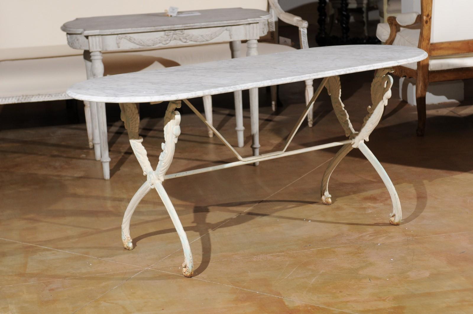 A French cast iron table from the 20th century, with oval Carrara marble top and swan motifs. Born in France during the 20th century, this cast iron table features an oval veined Carrara marble top sitting above an X-frame base adorned with delicate
