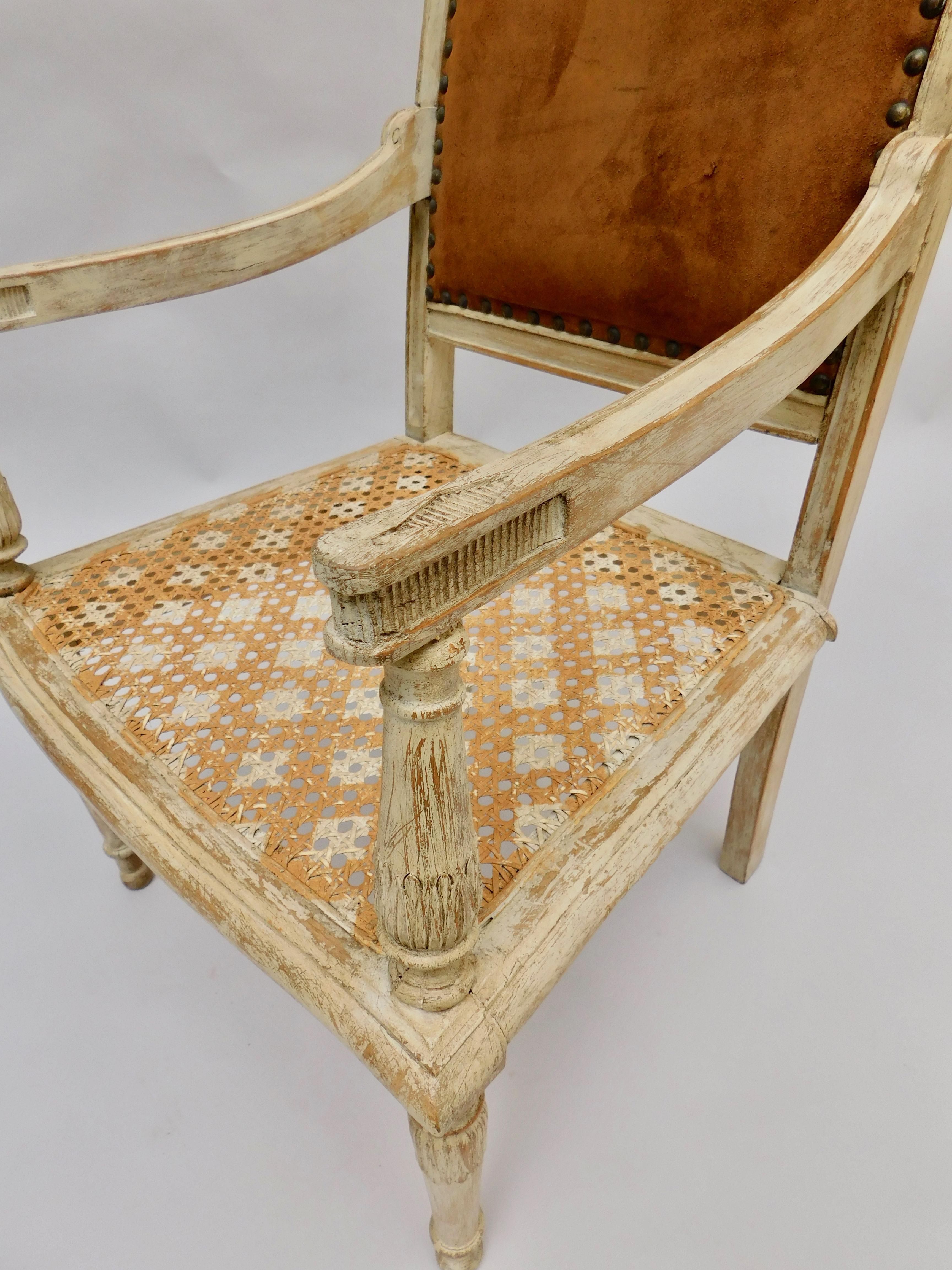 A most elegant children's armchair in the French Directoire style, circa 1890. Beautiful painted surface including the natural cane woven seat. The back retains the original caramel colored suede upholstery and brass studded nailhead trim.