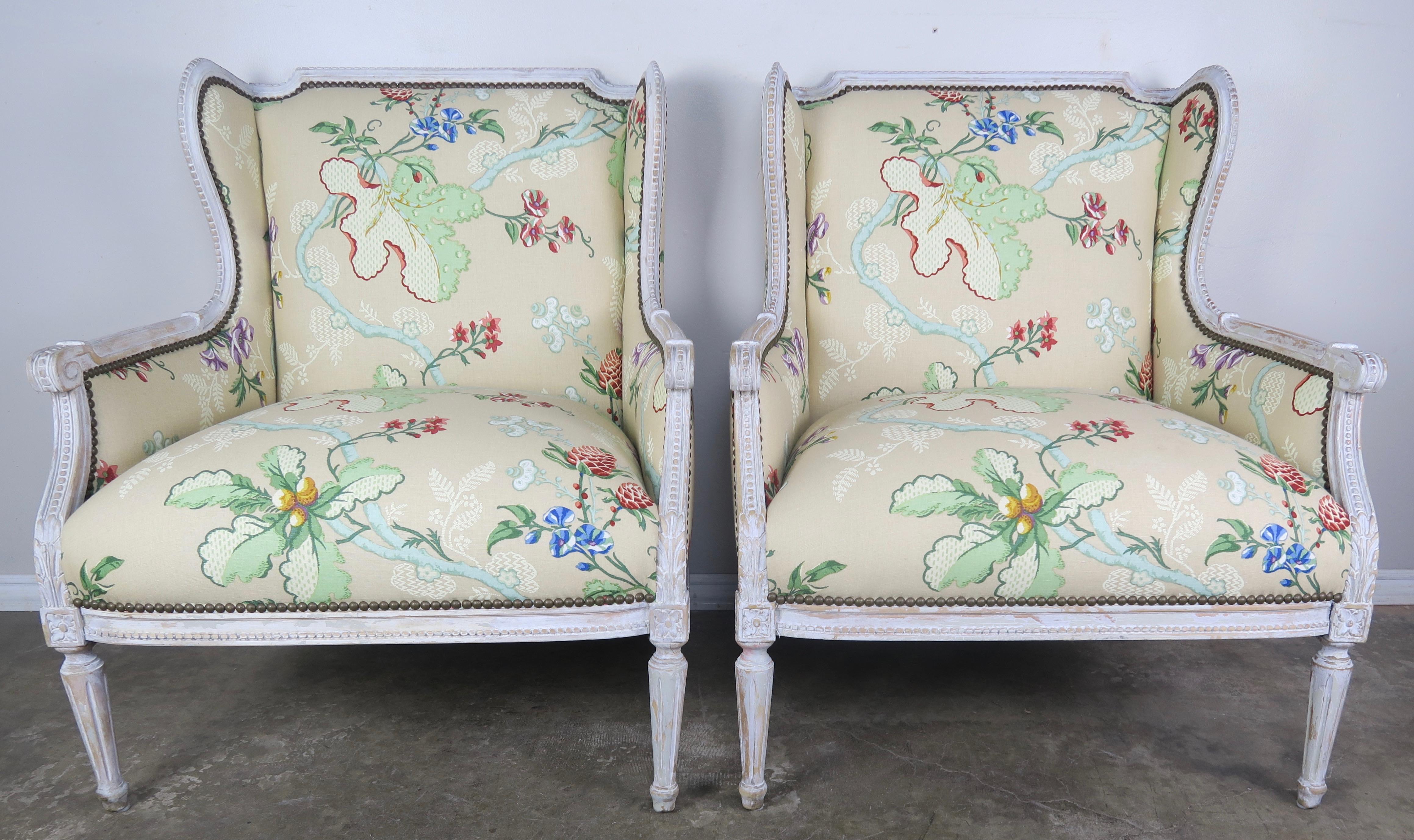 Pair of early 20th century French painted wingback armchairs standing on four straight fluted legs. The armchairs are painted in a French gray that is worn throughout exposing the wood underneath. The chairs are newly upholstered in a vintage (but