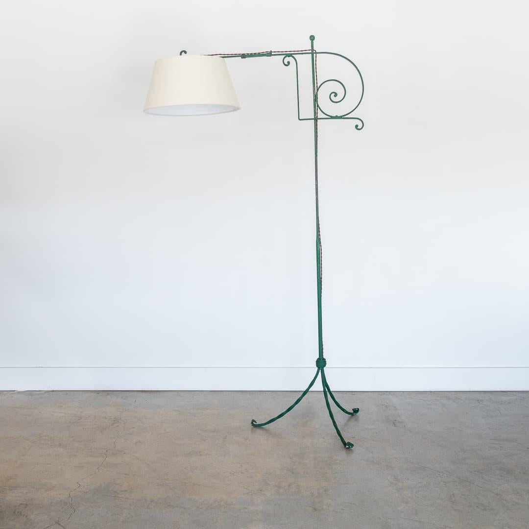 Stunning wrought iron floor lamp from France, 1940s. Beautiful painted green iron with twisted iron tripod base with thin stem. Beautiful scroll detail on bridge form arm. New linen tapered shade and newly re-wired. Unique and striking piece.