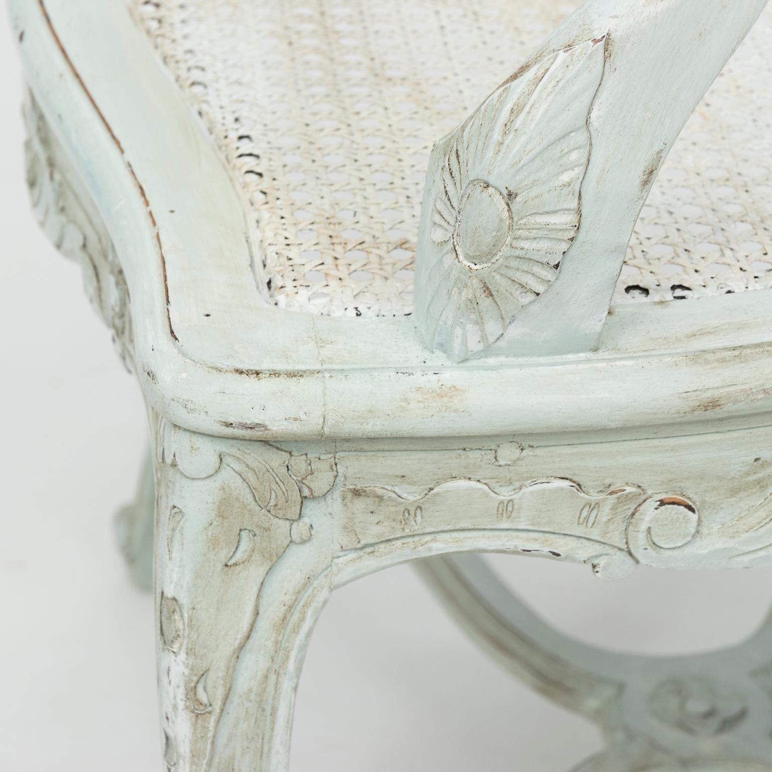 1950s white painted Louis XVI style armchair with cane woven seat and an X-shaped cross stretcher. The skirt and top rail also feature carved scallop shellwork with folliate trim.
 