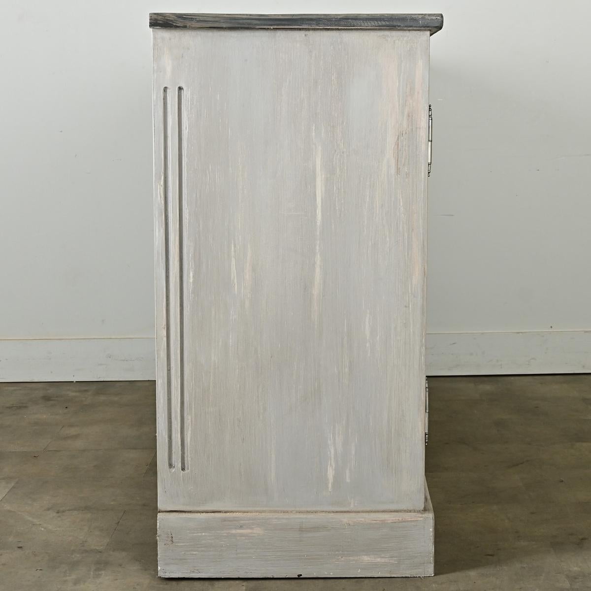 Reproduction d'une enfilade française de style Louis XVI peinte en gris, dans une texture patinée éthérée. Les portes à quatre panneaux sont rehaussées de rosettes dans chaque coin, ce qui adoucit les proportions linéaires de l'armoire. Trois