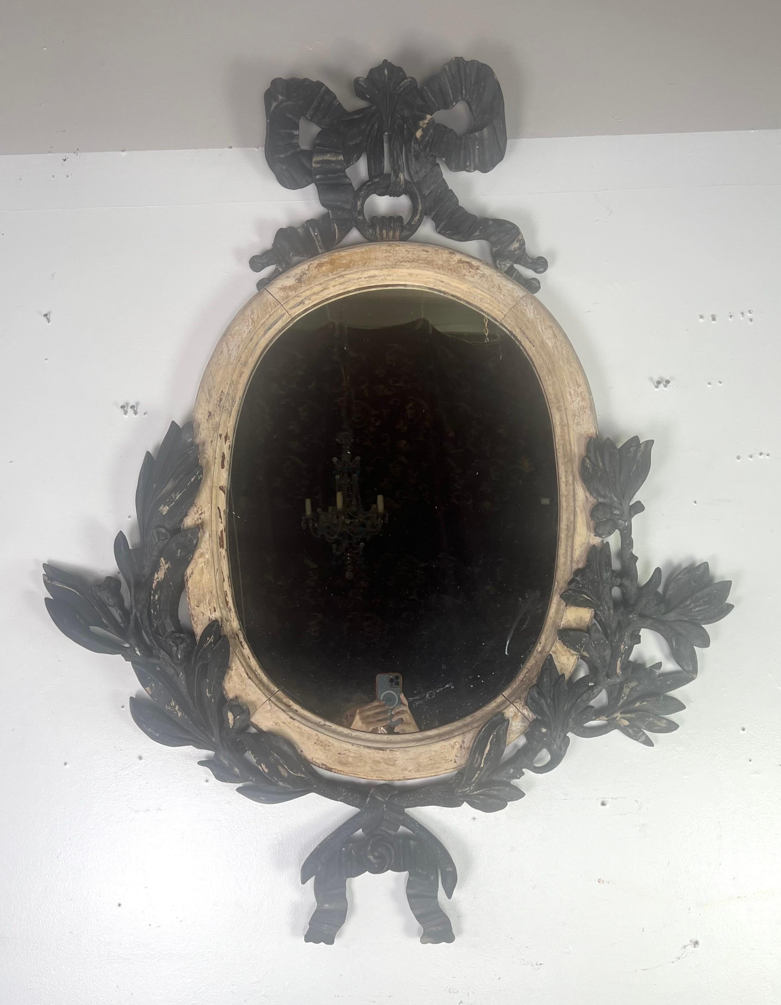 Miroir vintage français orné avec un cadre distinctif et décoratif.  Le miroir est de forme ovale, ce qui ajoute une touche classique et élégante.  Le cadre est en bois, avec une finition vieillie qui lui donne un aspect altéré.  La partie