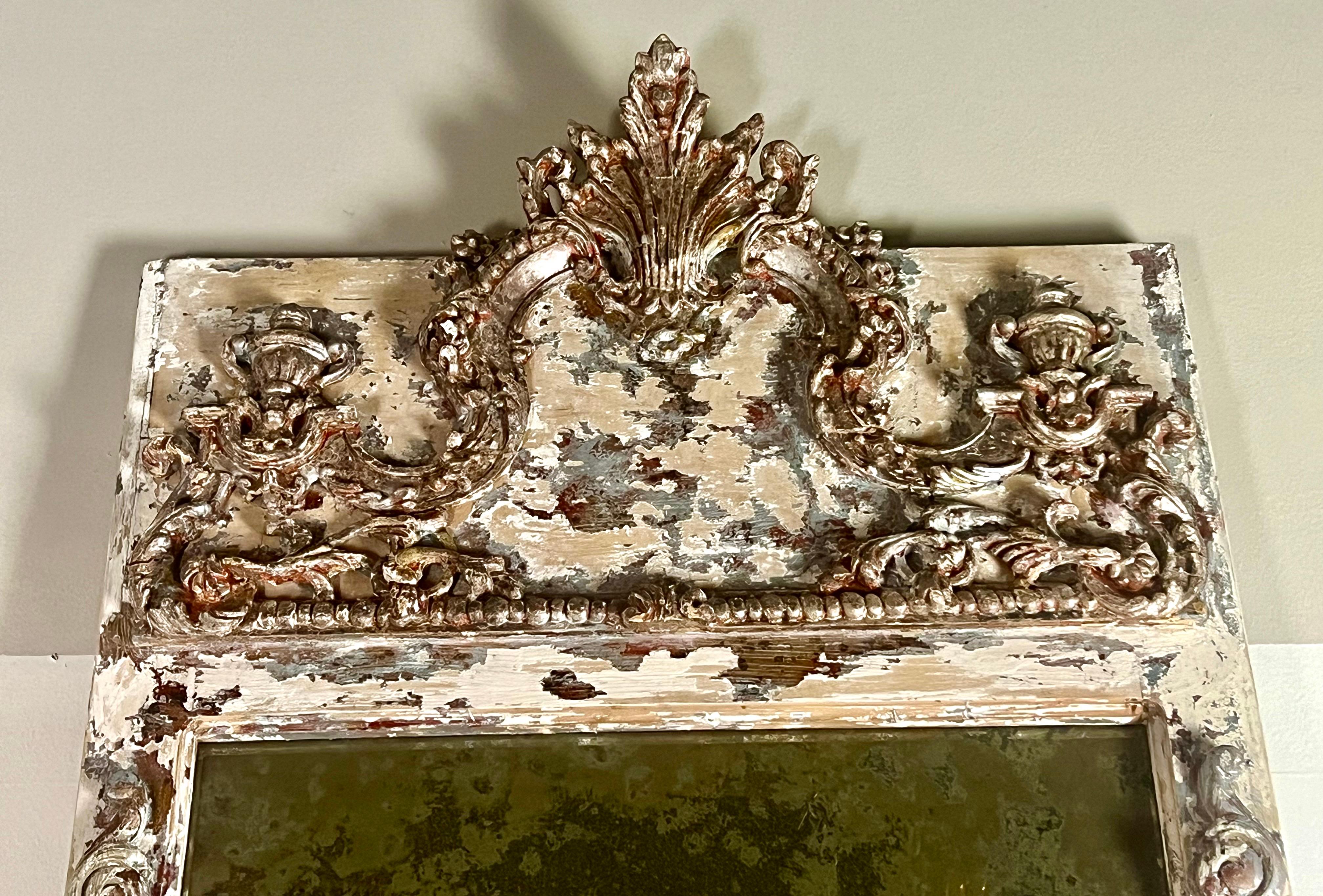 French trumeau mirror with cream paint and silver gilt accents, featuring a cartouche, acanthus leaves, and small urns, all rendered in a beautifully weathered finish.
