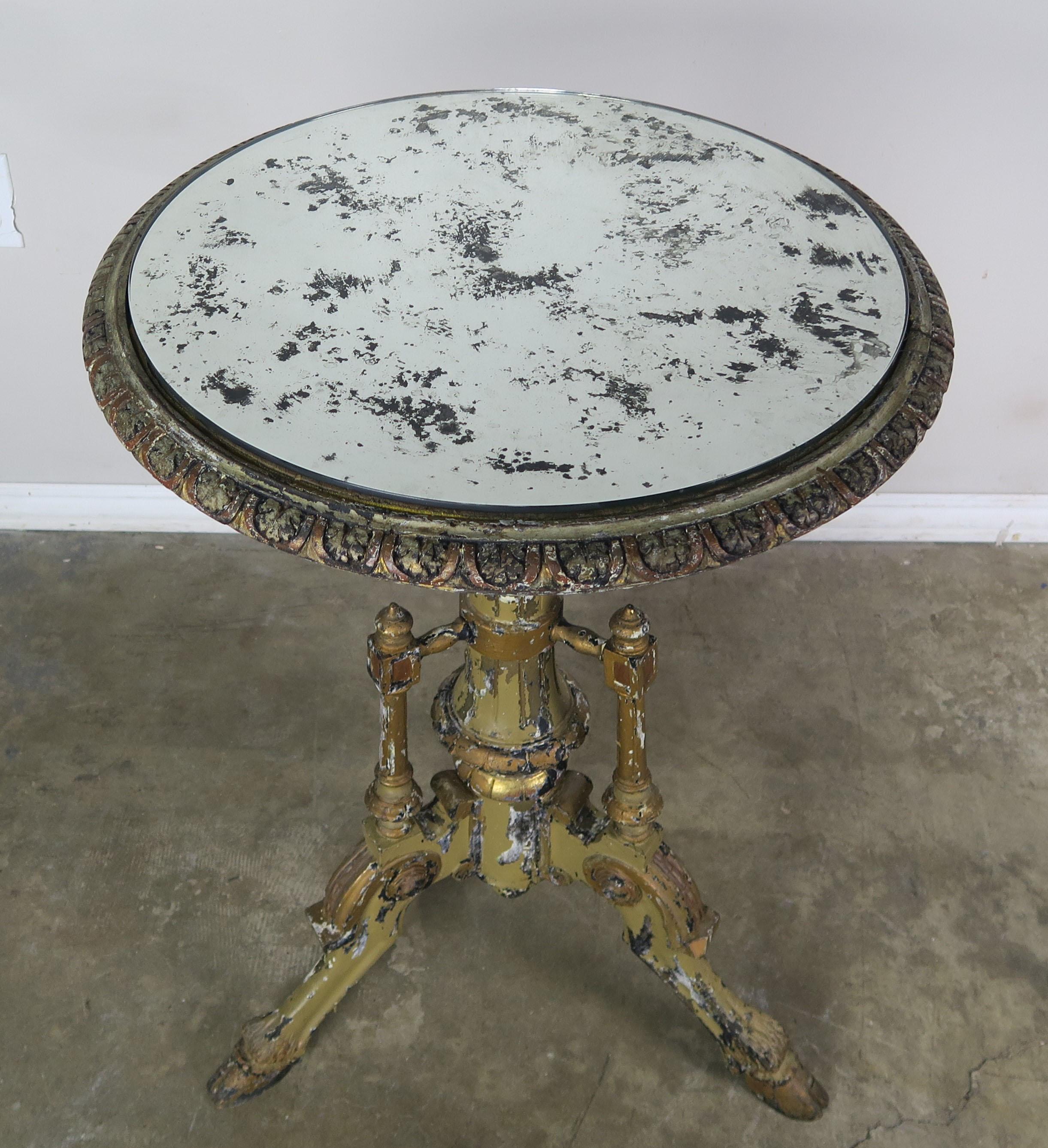 French painted side table with an antiqued mirrored top. The table stands on a tripod base with three legs ending in carved hoofs. The table has a beautifully carved apron on it's top that holds a great antique mirrored top.