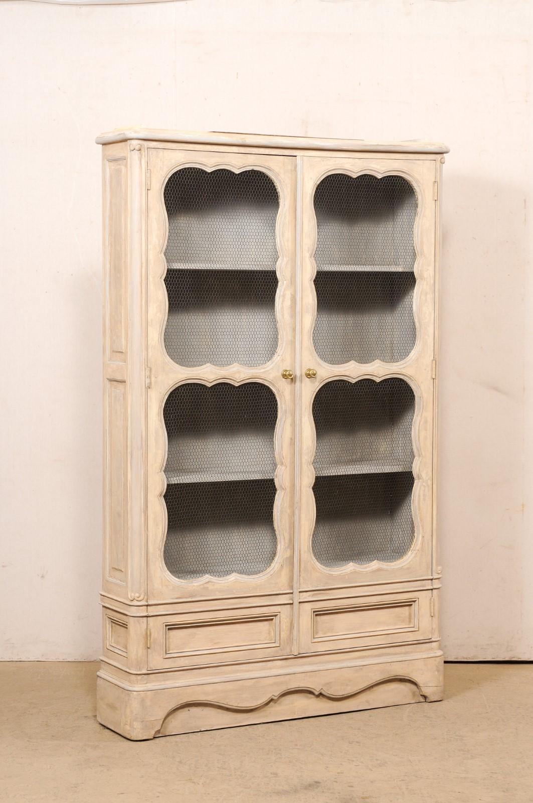 A French carved and painted wood bookcase, with wire door fronts, from the mid 20th century. This vintage display cabinet from France, standing approximately 6.75 feet in height, is fitted with a pair of decoratively scallop-carved panel doors with