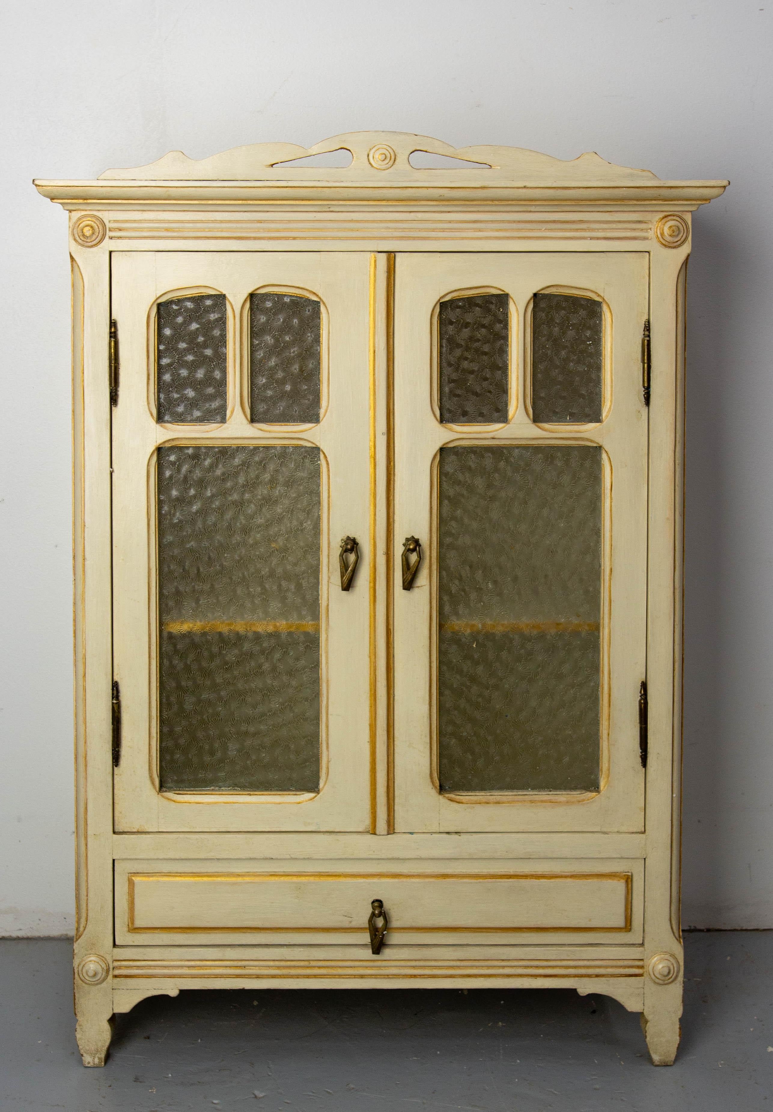 French small armoire with two glass doors and a drawer. 
The shape of the cabinet is inspired by Art Nouveau, but the handles are from the Art Deco period, when the cabinet was made and painted.
Please note the small signature initials made by the