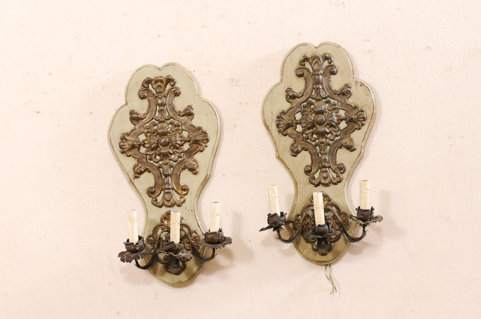 A French pair of 19th century sconces mounted on shapely carved and painted wood back-plates. This antique pair of sconces from France have been fashioned from 19th century brass/metal fixtures consisting of elaborately designed metal plaques, metal