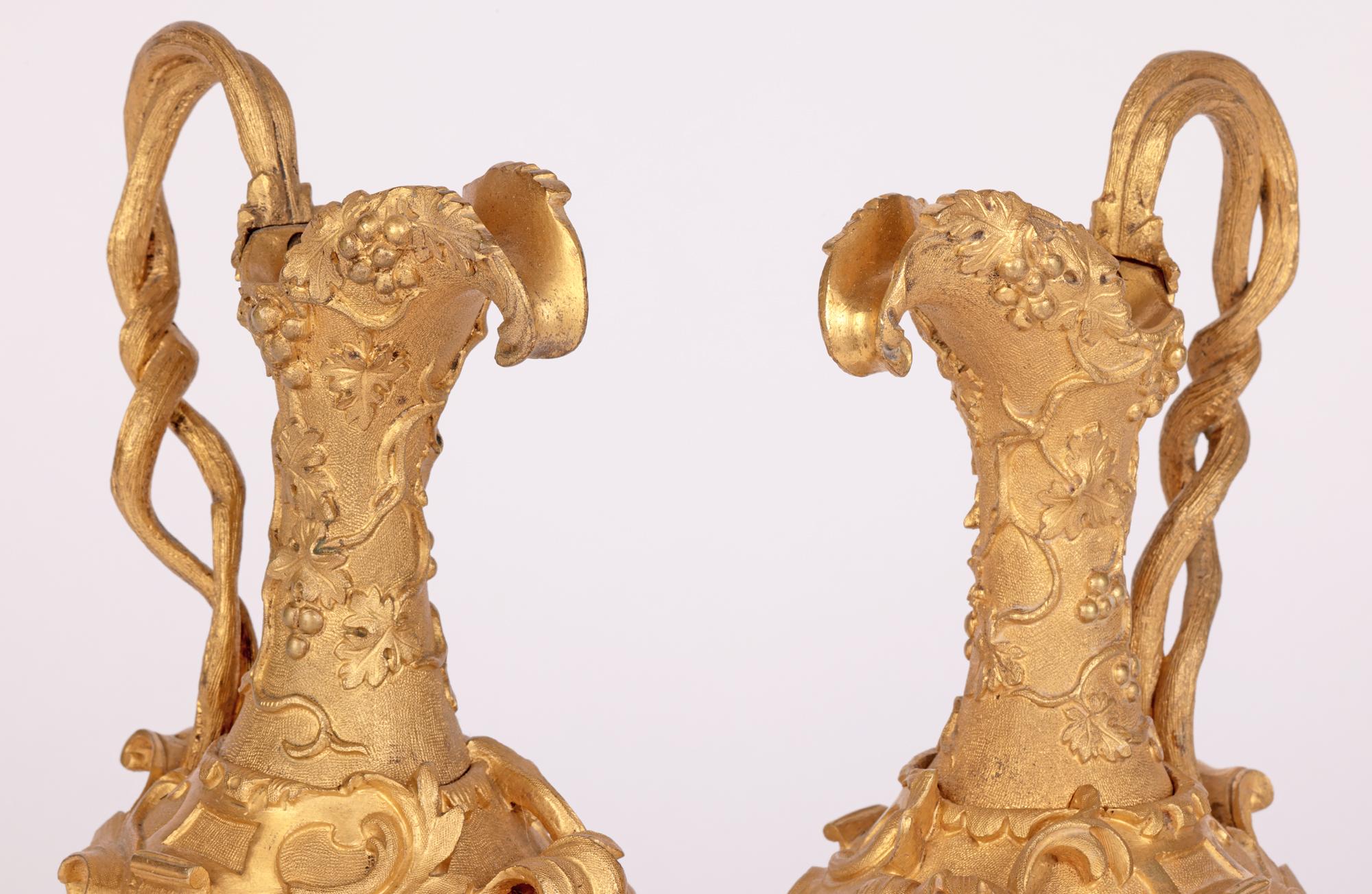 A very fine pair antique French neo-classical gilded bronze ornamental ewers applied with scroll and vine designs dating from the 19th century. The ewers stand on a scroll and molded shell decorated rounded base with column form stems support