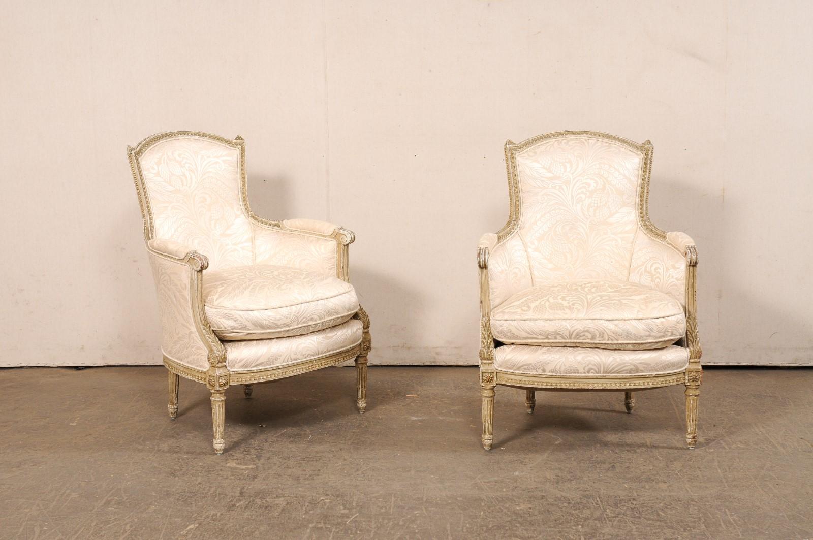 A French pair of Louis XVI style occasional barrel-back bergère chairs from the early 20th century. These antique tub chairs from France have beautifully rounded backsides, with a subtly arched top rail flanked within petite should finials; all