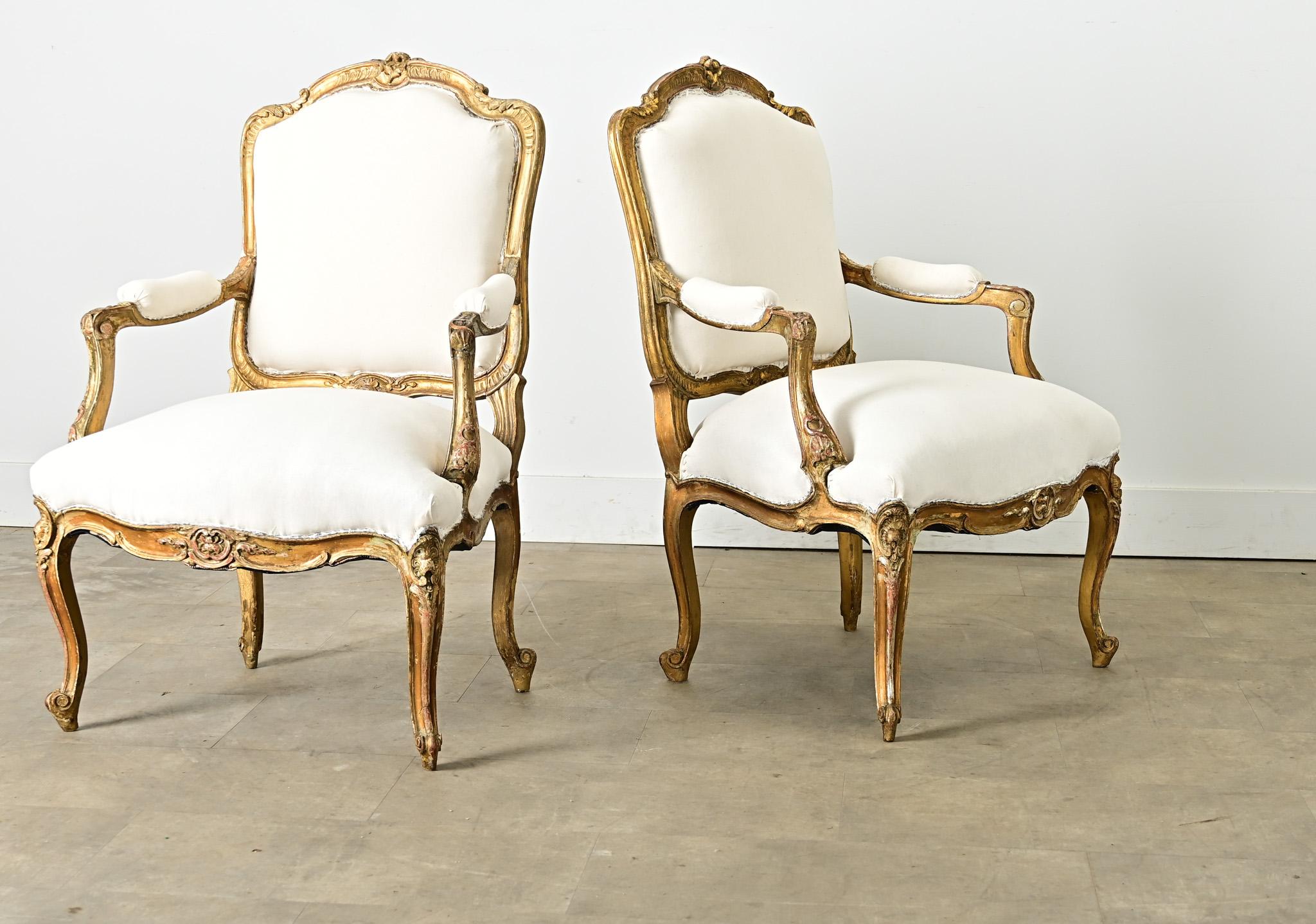 Une paire intemporelle de fauteuils dorés fabriqués en France à l'époque Louis XV, reflétant l'opulence romantique de l'époque et tempérée par la patine développée au cours de trois siècles. Ces fauteuils ont un cadre sculpté incorporant des motifs