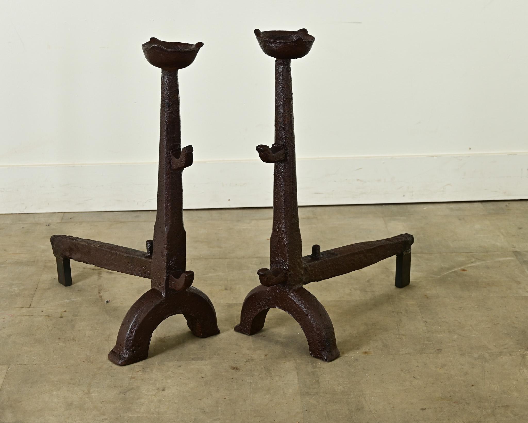 A monumental pair of French hand-forged, wrought iron fireplace andirons, made in the 18th century if not earlier. They are Gothic in style with a reddish brown patina from oxidation of the iron and centuries of exposure to high heat. The hefty
