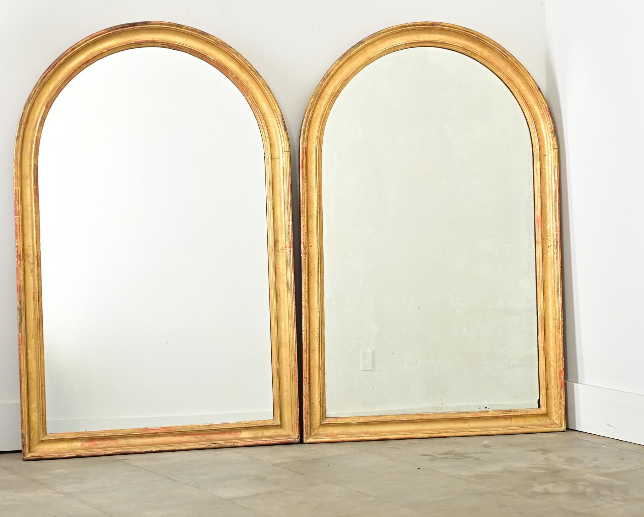Preciosa pareja de espejos dorados procedentes de la Francia del siglo XIX. Las fuertes proporciones de los marcos arqueados se ven acentuadas por la arcilla roja que asoma a través del reluciente dorado. Las molduras sobrias son lisas y