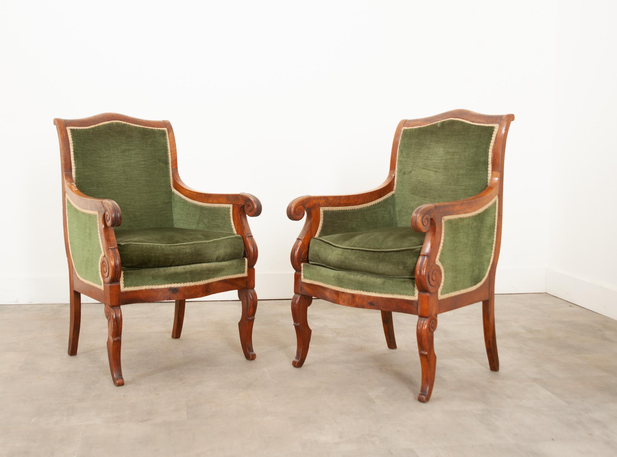 This flirty pair of French walnut bergeres is in wonderful antique condition. The frames are 19th century, hand carved with a deep trim and scrolling arms. Upholstered in plush emerald green velvet with a gold rick rack trim with additional
