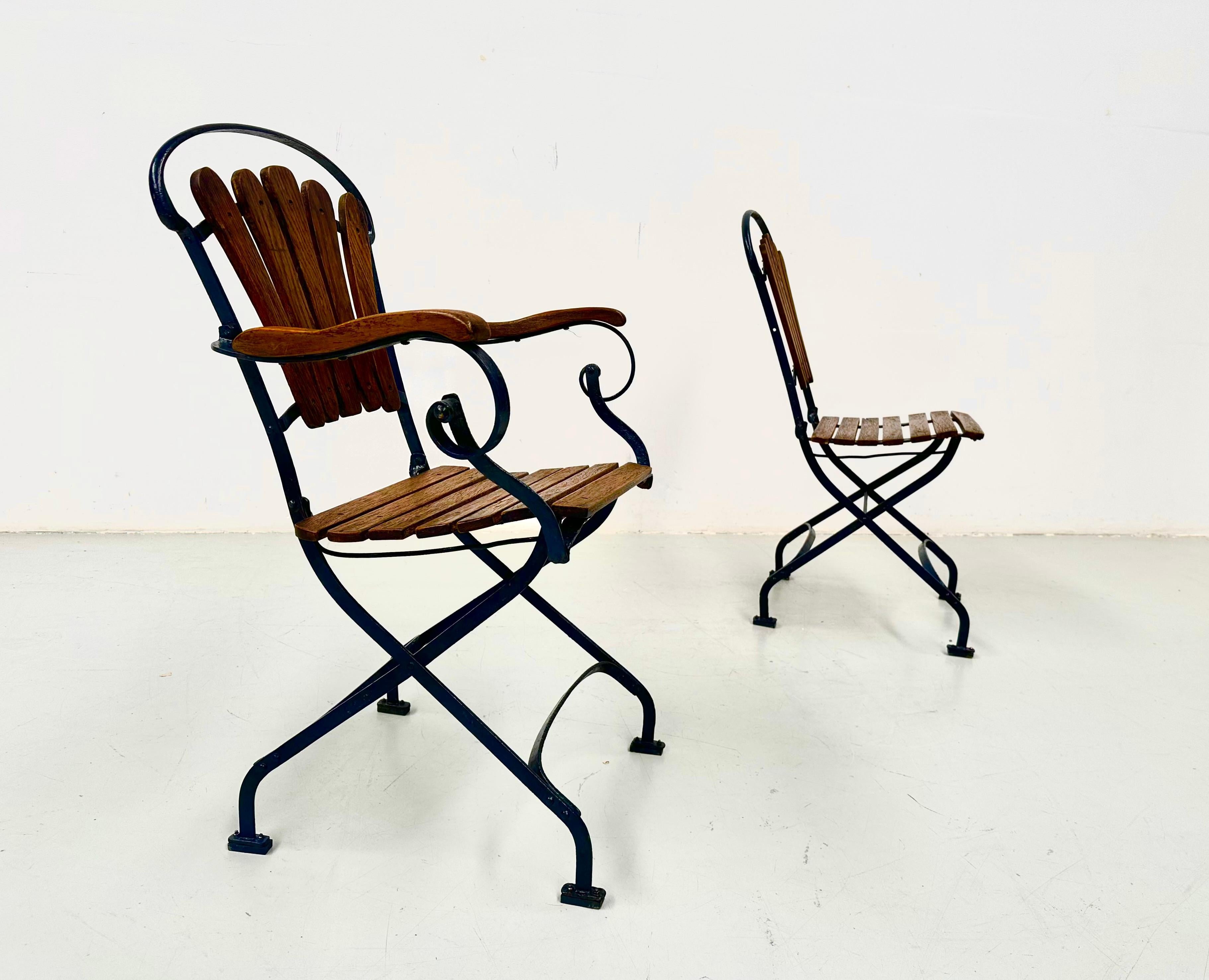 Cette paire de chaises de bistrot anciennes en fer forgé bleu et en bois de chêne a été fabriquée dans les années 30 en France. L'ensemble est remis à neuf et vérifié dans notre atelier. Les anciens panneaux de bois usés ont été remplacés par de