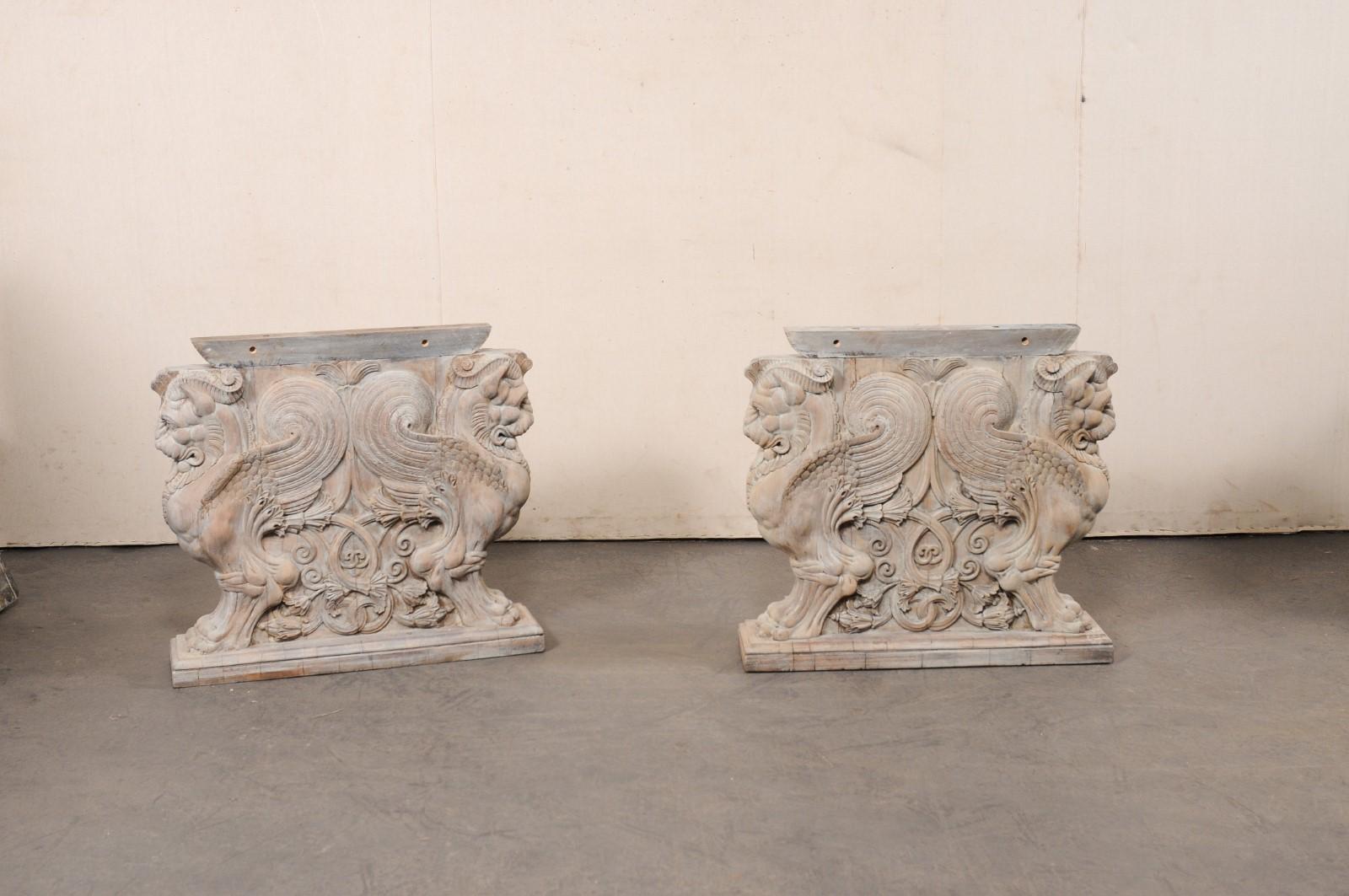 A fabulous French pair of wall consoles, with griffin carved-wood pedestal bases, from the turn of the 19th and 20th century. These antique tables from France each have a rectangular-shaped top, which is raised upon a wood base that features a pair