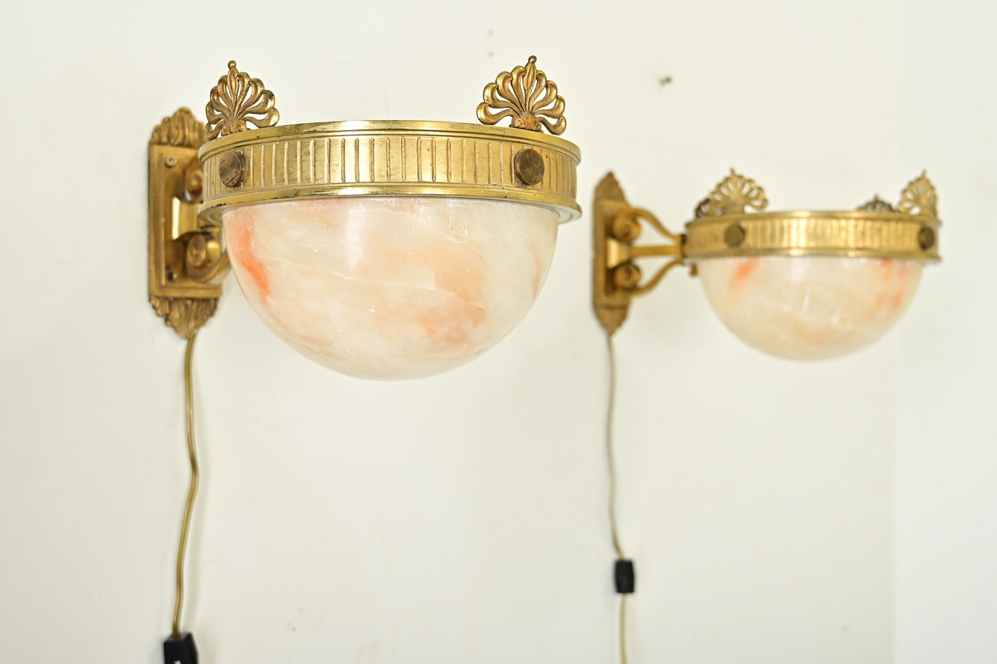 Eccezionale coppia di applique francesi in stile Art&Deco con diffusori in alabastro intagliato appesi a cornici in ottone. Le piastre posteriori sporgono dalla parete come due volute intorno al palo quadrato, il che implica un design a lira.