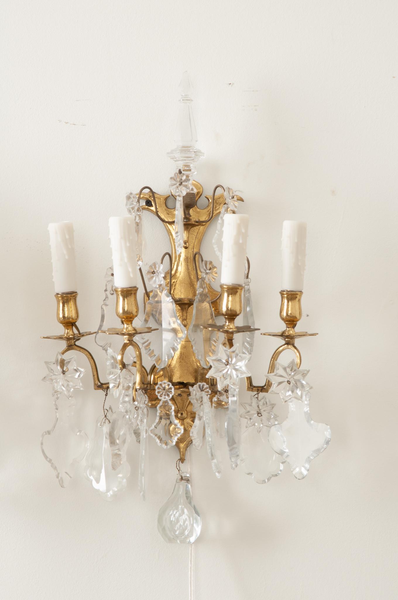 An elegant pair of brass and crystal French wall sconces. Each sconce has four brass arms with cut crystals all ending on a vertical cut brass backplate. The pair have been cleaned and wired for US electrical using UL certified parts. The backplates