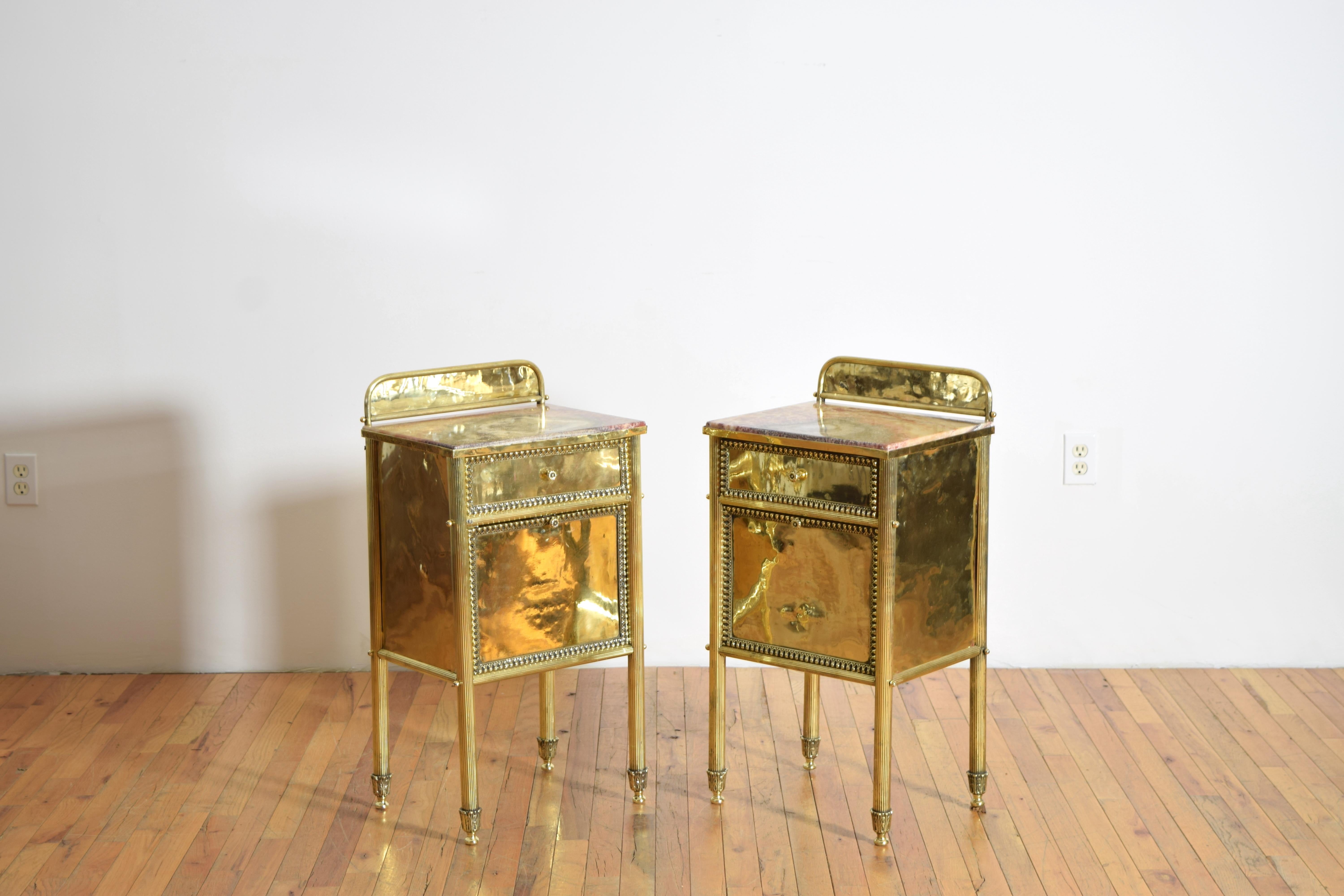 constructed entirely of brass with rectangular inset onyx tops the frames having raised backsplashes, the cases each with one drawer and a door and raised on fluted tapering legs terminating in shaped feet, height of tabletop is 27.25