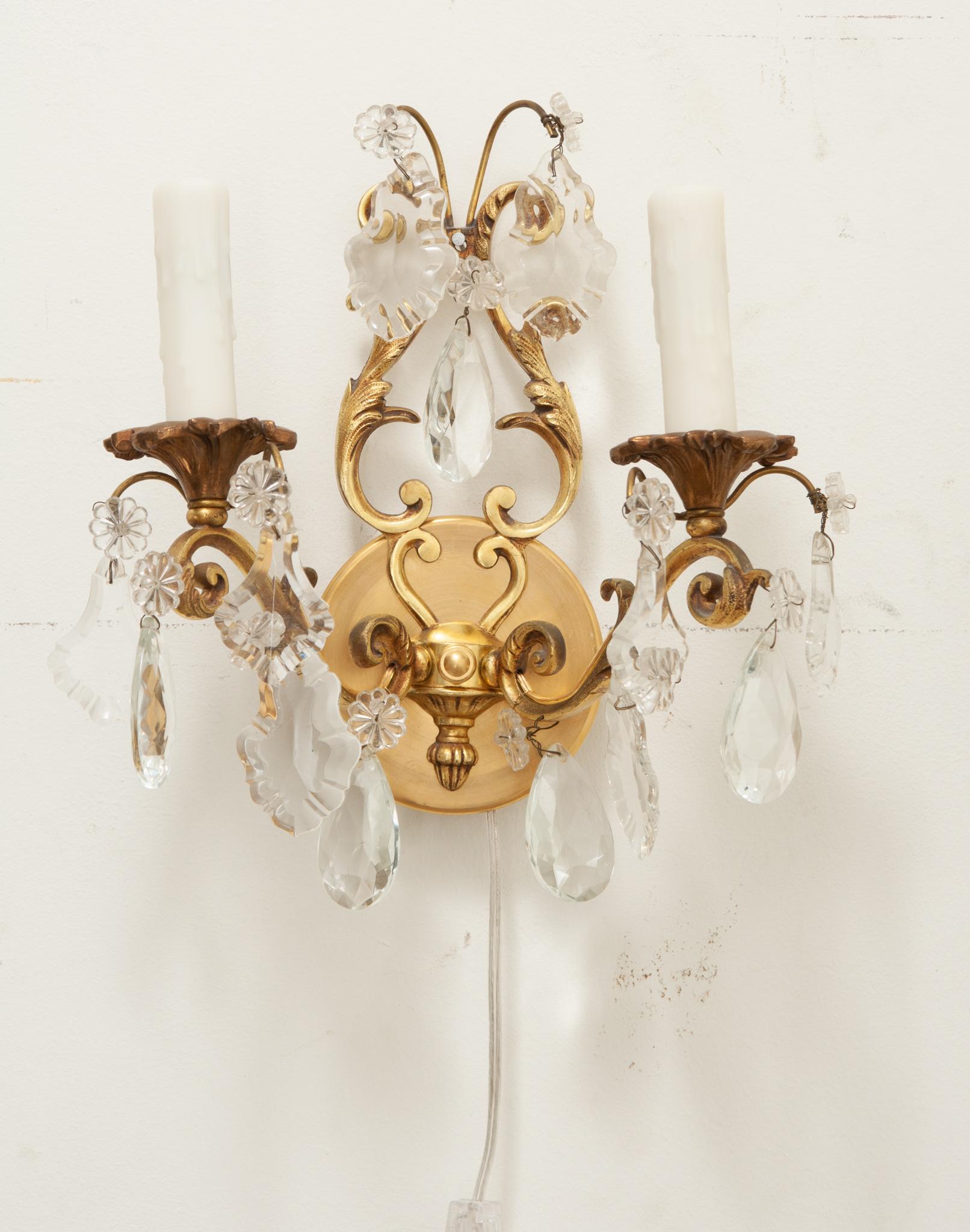 An elegant pair of petite brass and crystal French wall sconces. Each sconce has two brass arms with faux candle covers and cut crystal drops. The pair have been cleaned and wired for US electrical using UL certified parts. Be sure to look at the
