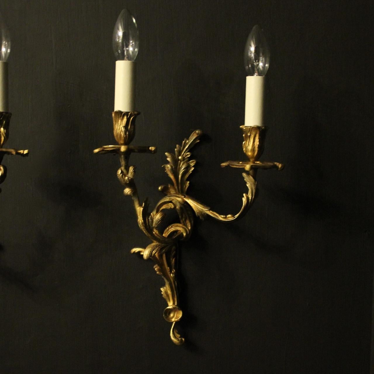 A French pair of gilded bronze twin arm opposing antique wall sconces, the leaf scrolling arms with leaf bobeche drip pans and candle sconces, issuing from a decoratively cast opposing leaf backplate, good original colour and well cast. Fully