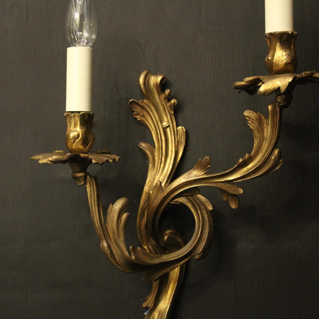 A French pair of gilded bronze twin arm opposing antique wall sconces, the leaf scrolling arms with leaf bobeche drip pans and bulbous candle sconces, issuing from a decoratively cast opposing leaf backplate, nice original color. Fully rewired and