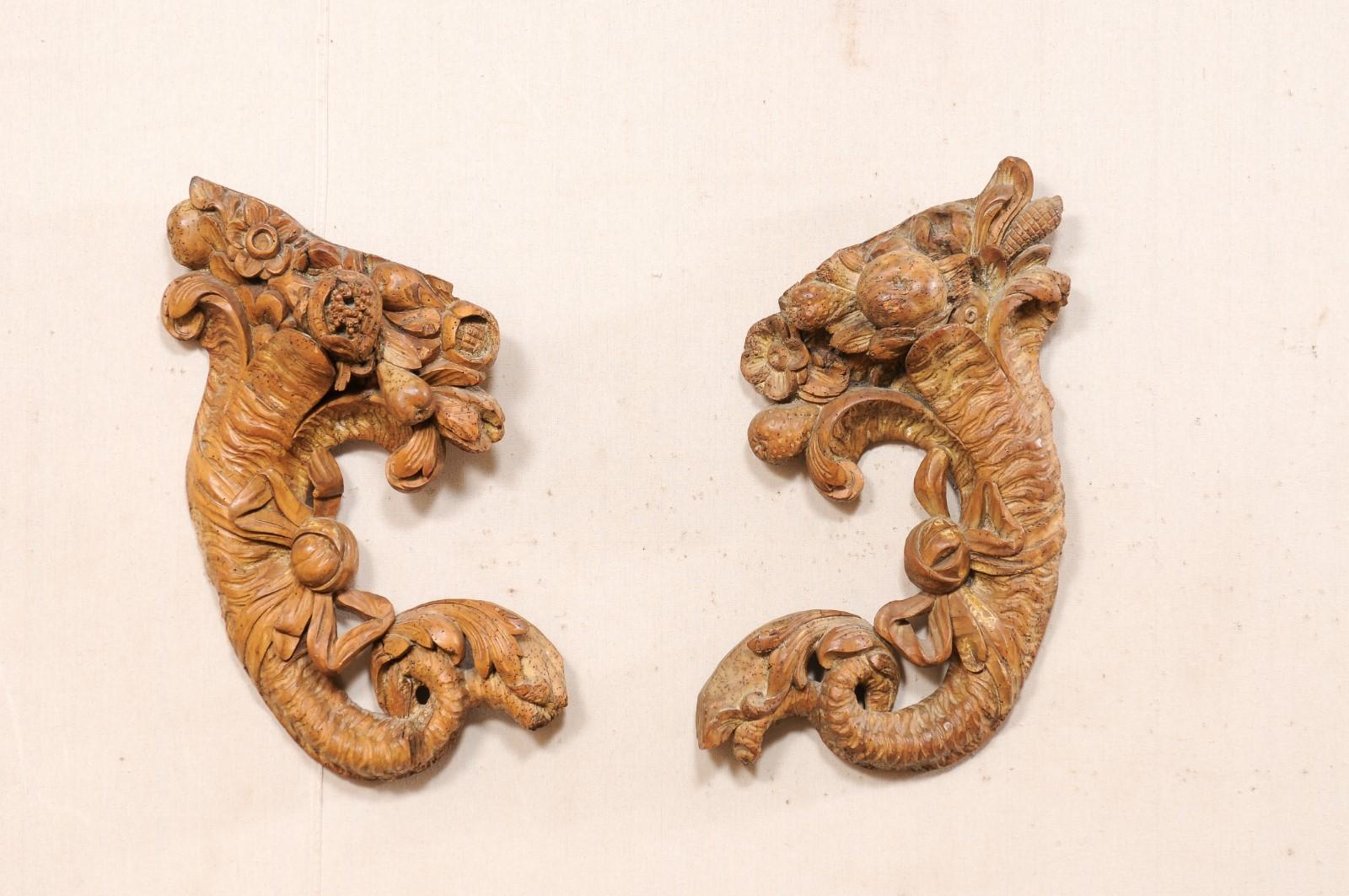 A French pair of carved-wood cornucopia wall decorations from the turn of the 18th and 19th century. This antique pair of wall plaques from France have each been hand-carved, depicting cornucopias filled with flowers and bow-tied ribbons at their
