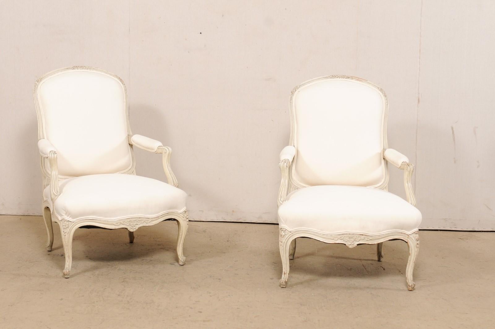 Paire de fauteuils en bois sculpté du début du 20e siècle. Cette paire de fauteuils anciens, originaires de France, présente des traverses supérieures légèrement arquées, sculptées d'un délicat motif floral, des accoudoirs aux manchettes paddées et
