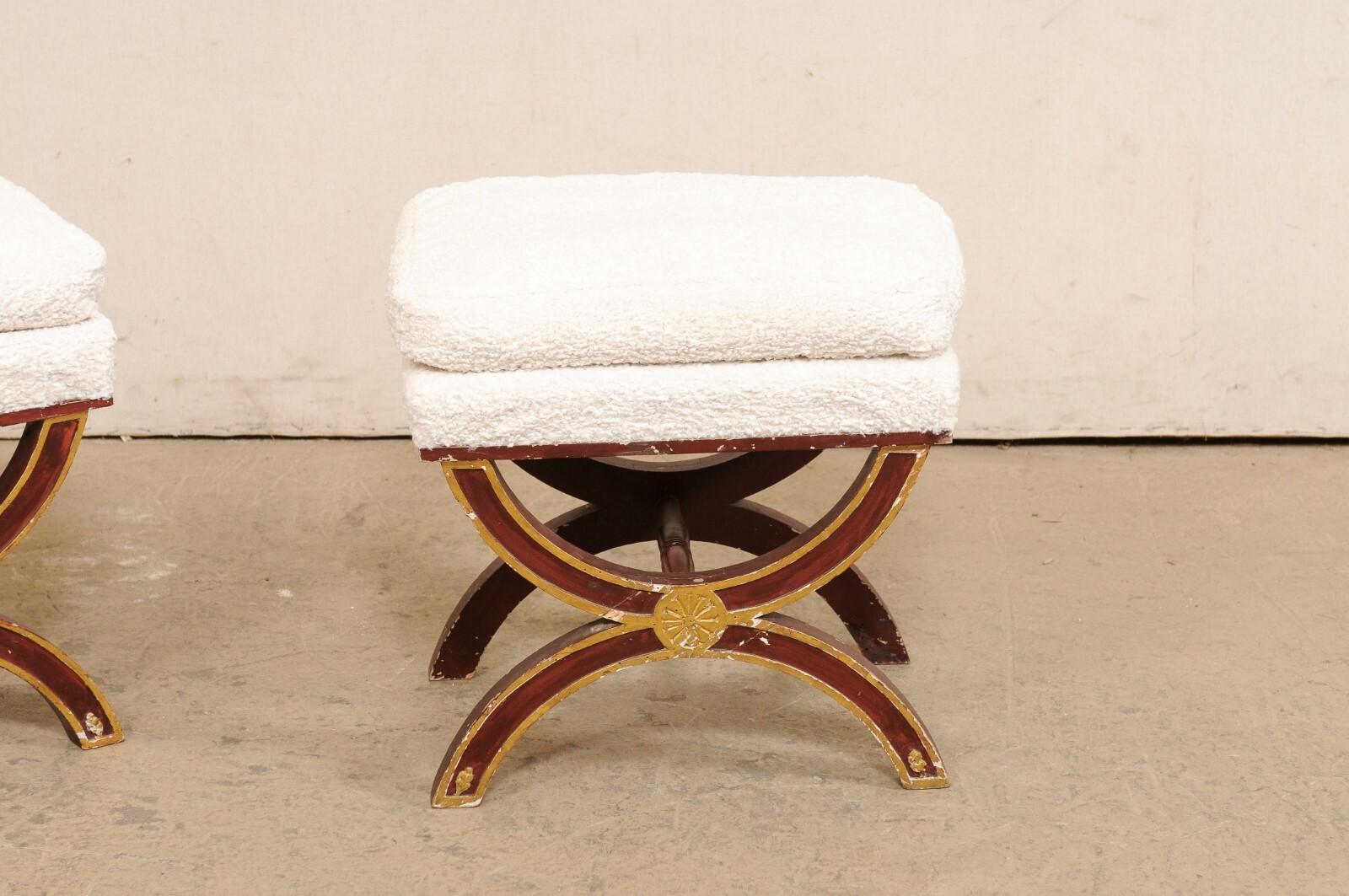 A French pair of wooden curule style stools, with upholstered seats. These vintage stools from France have been created in the Curule (or often referred to as Dante) style, featuring legs comprised of opposing two half-moon shapes, which attach at