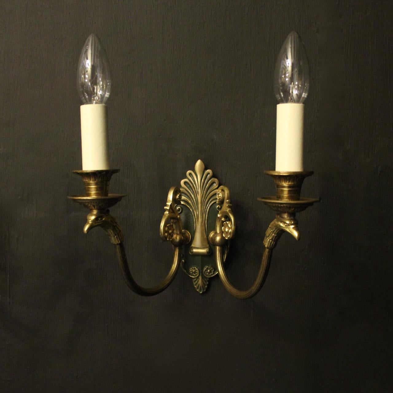 A French pair of Empire gilded bronze twin arm antique wall lights, the eagle headed reeded scrolling arms with circular bobeche drip pans and etched candle sconces, issuing from a central decorative dark green enameled backplate with Anthemion