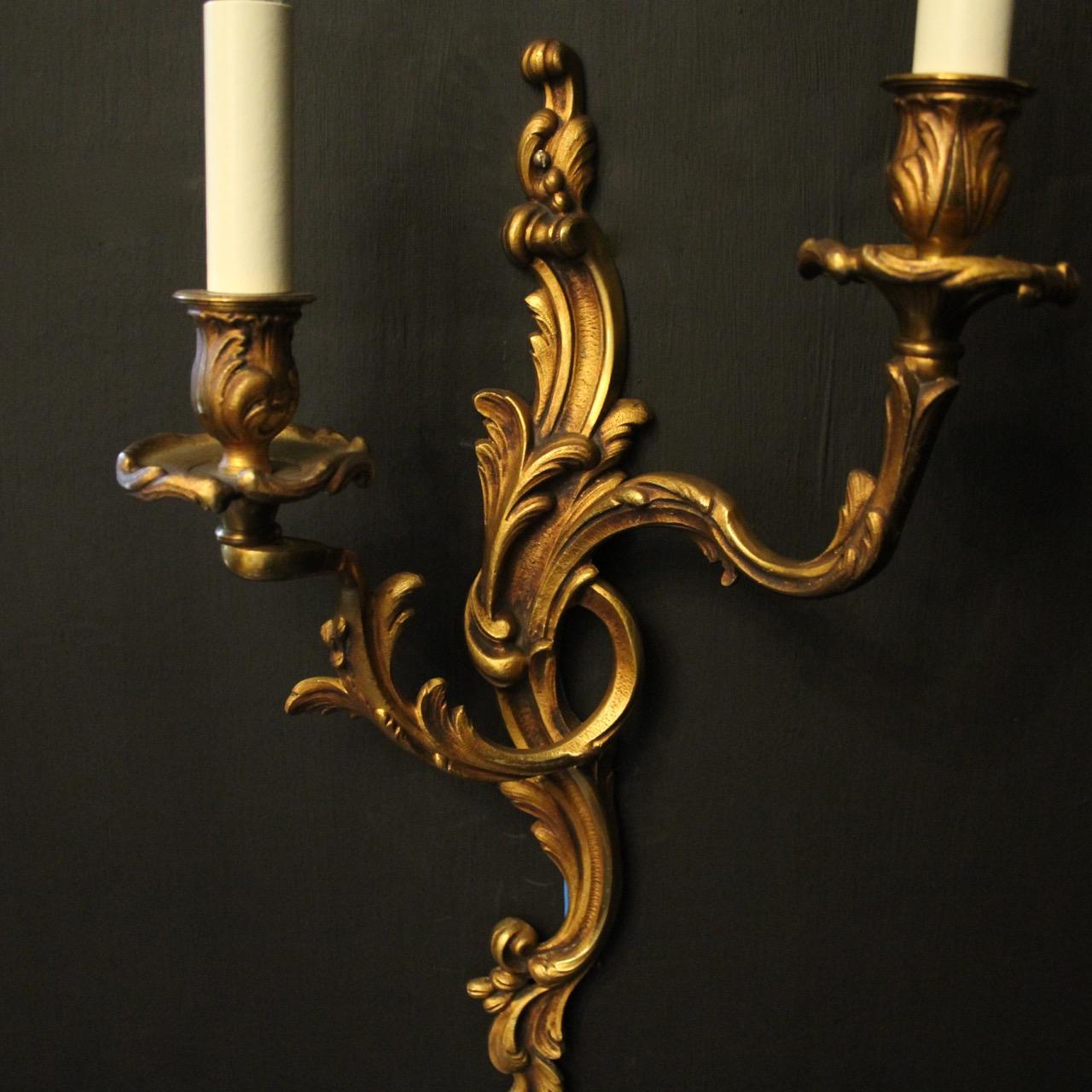 A French pair of gilded bronze twin arm opposing antique wall lights, the leaf scrolling arms with leaf bobeche drip pans and bulbous candle sconces, issuing from an opposing leaf elongated backplate, nice original gilded patination and great large