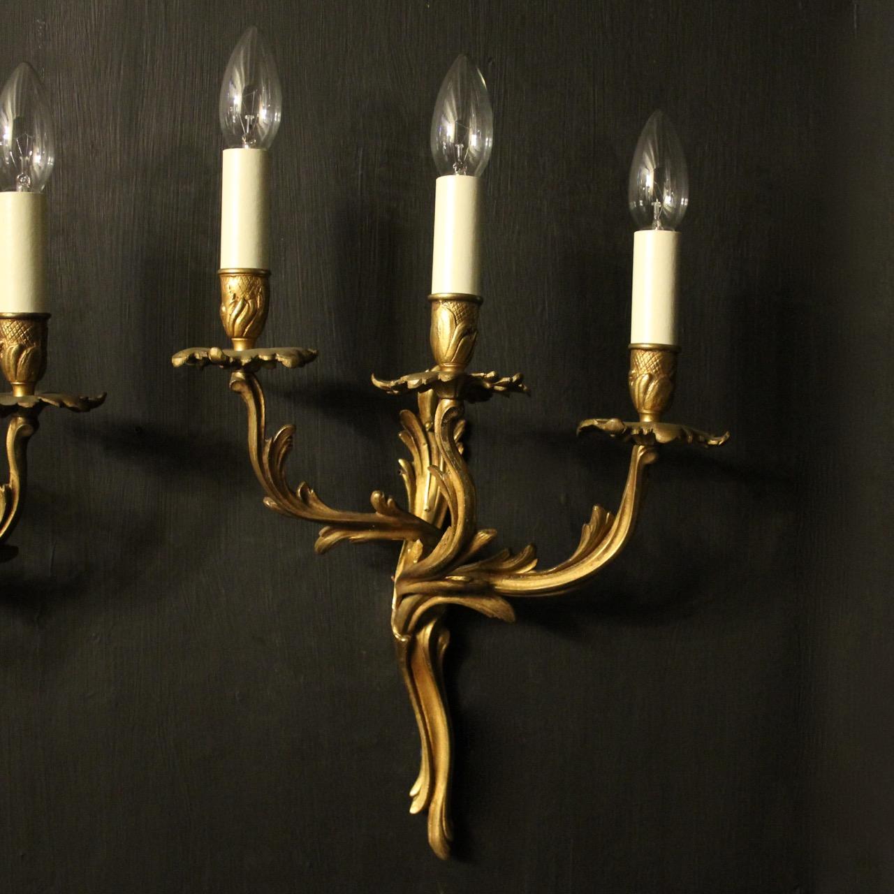 A French pair of gilded brass triple arm opposing antique wall lights, the leaf clad scrolling arms with leaf bobeche drip pans and bulbous candle sconces, issuing from an opposing leaf backplate, nice original patination and good scale. Fully